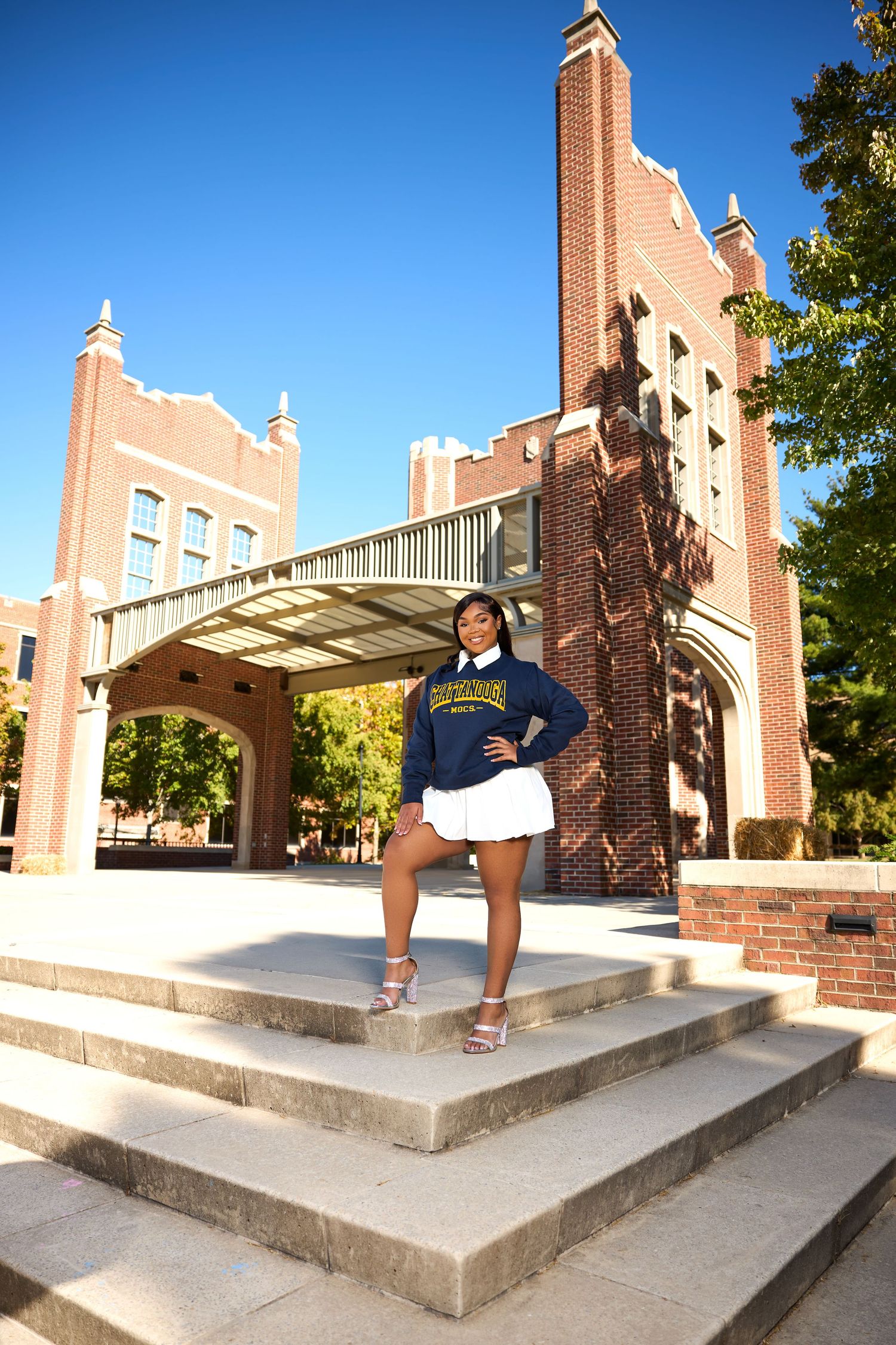 A student in university apparel poses confidently on stone steps in front of a collegiate building entrance.
