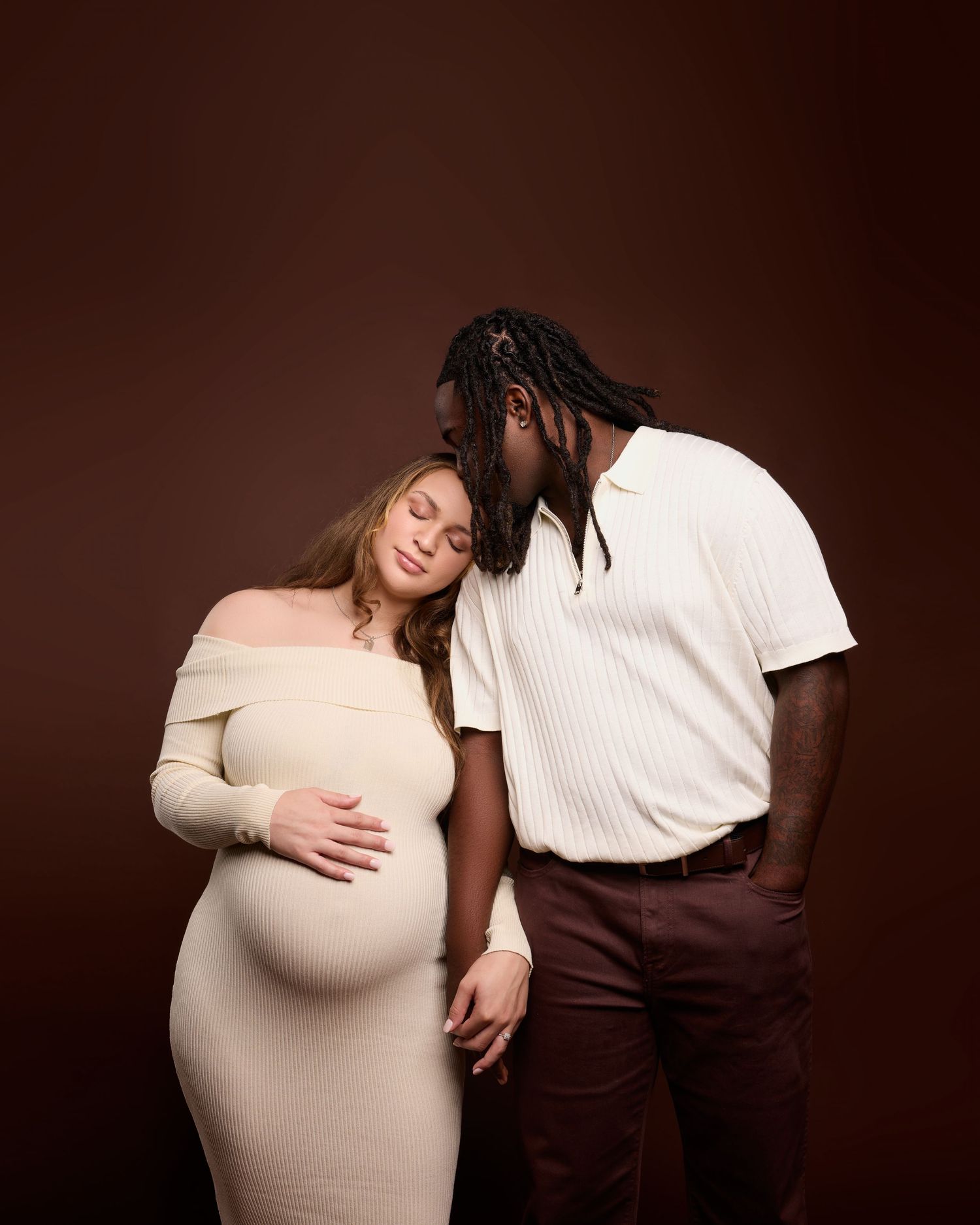 Maternity photo series with couple in cream and brown clothing against dark backdrop.