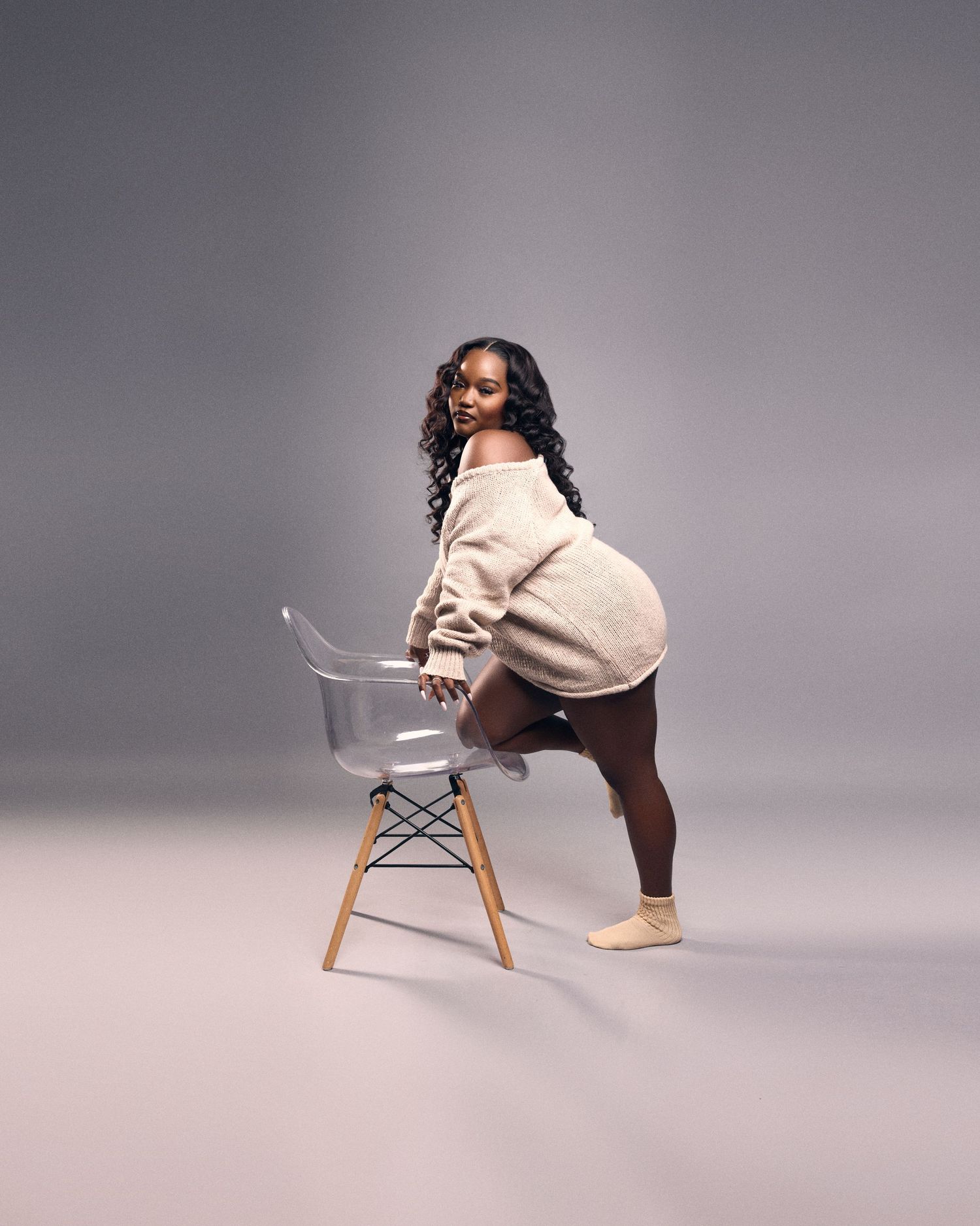 Fashion editorial with modern chair and cream sweater against grey backdrop.