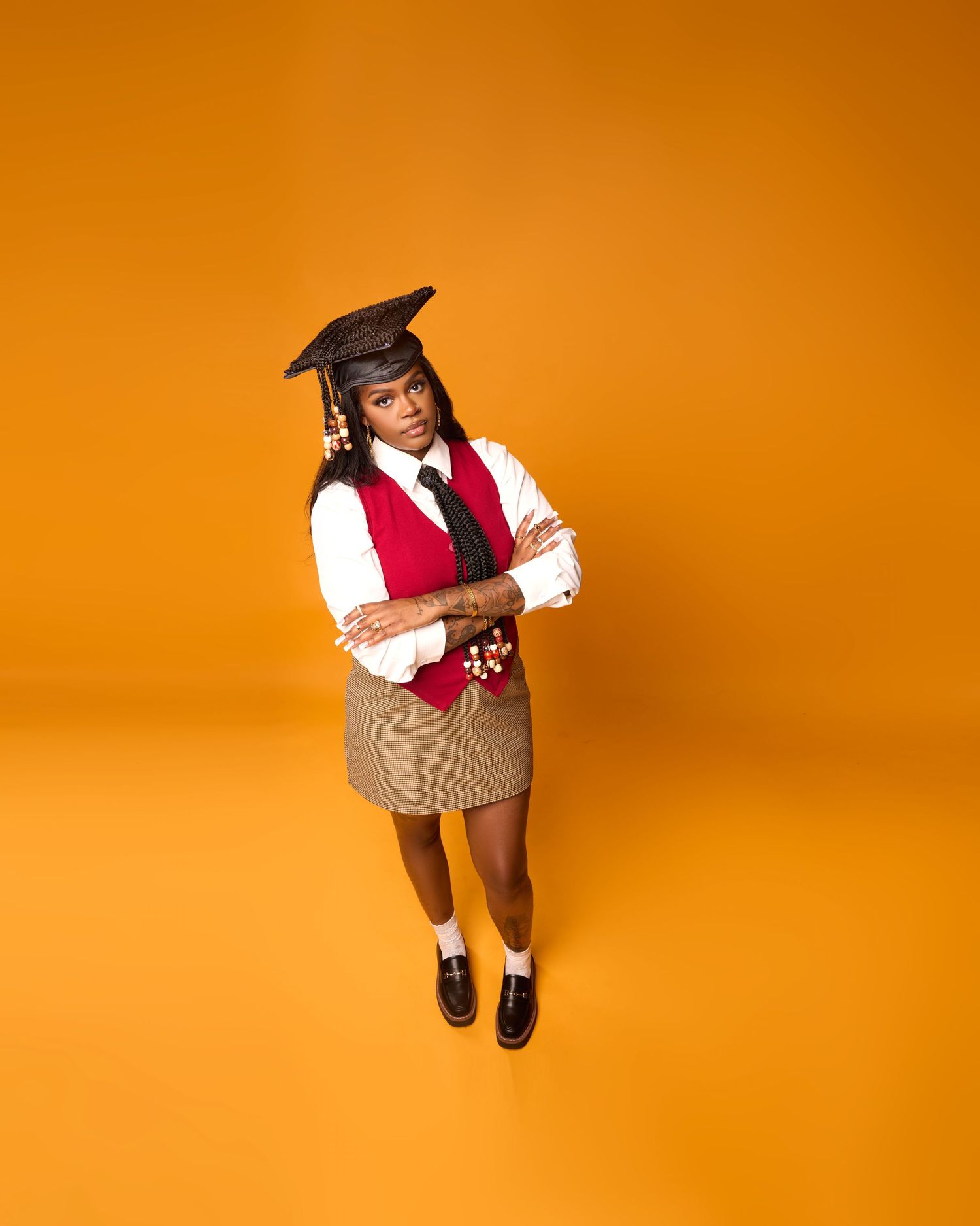 Graduate in cap and vest strikes dynamic poses on orange studio backdrop.