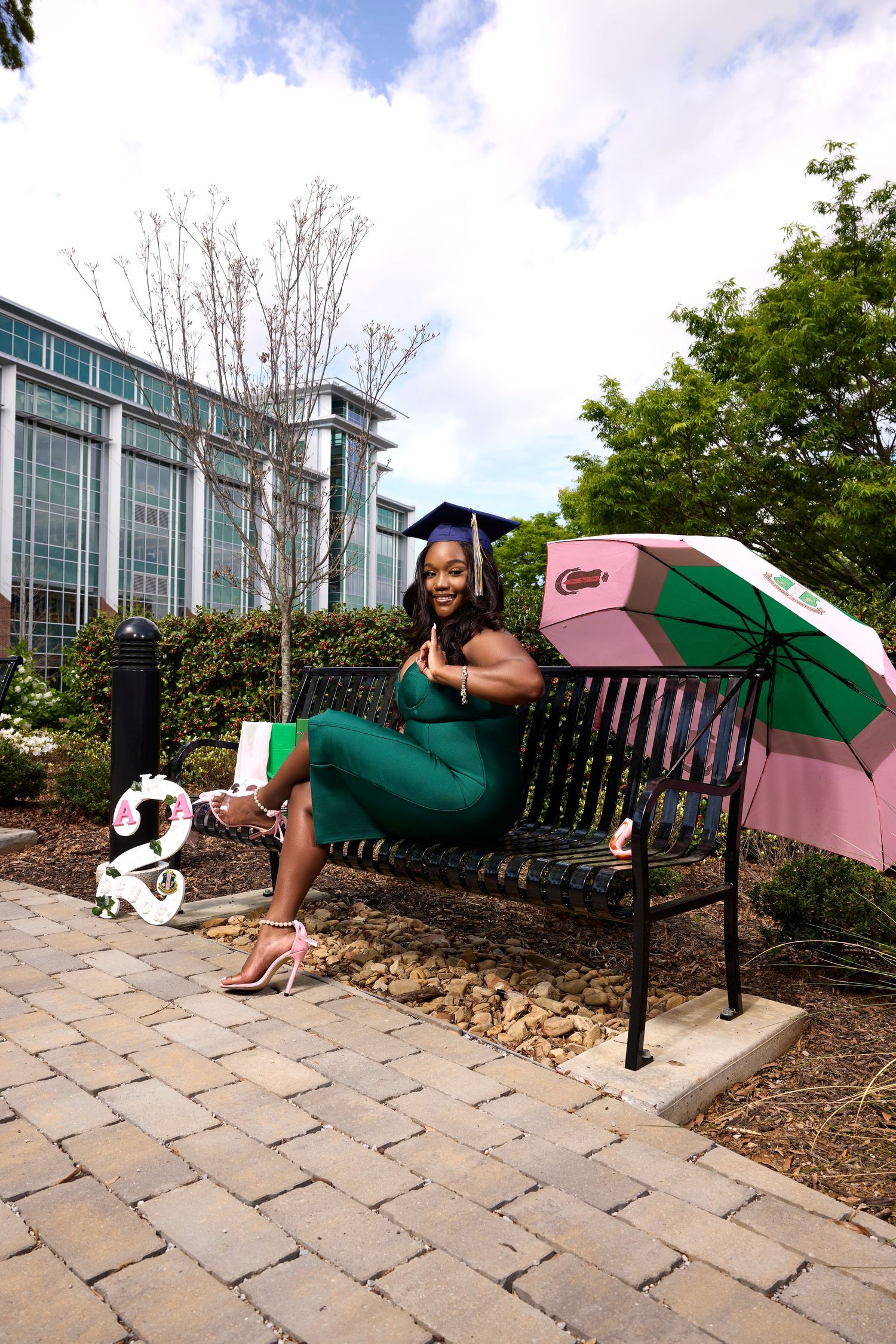 A graduate relaxes on campus bench with decorative umbrella and small mascot statue.