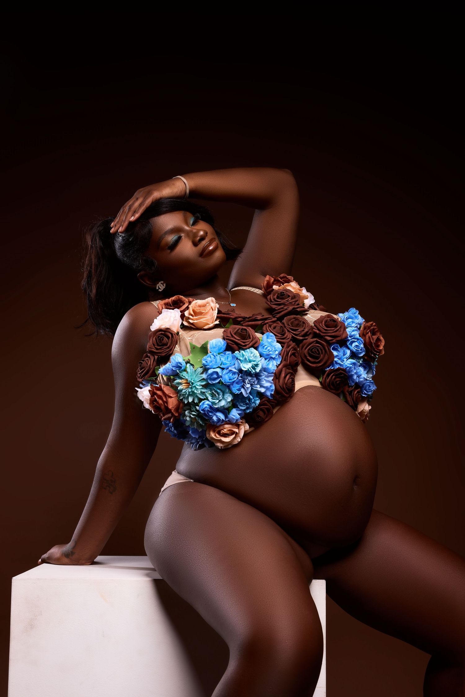 A maternity photoshoot featuring blue and brown floral decorations against a dark background.