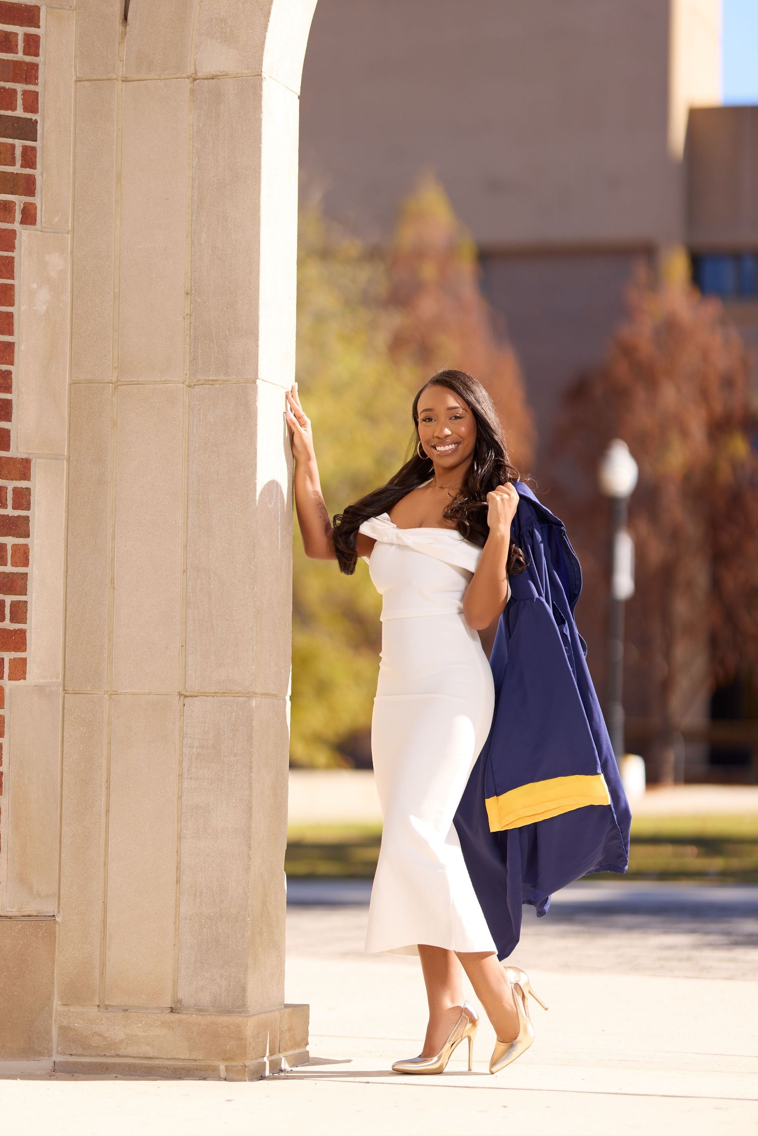 Joyful graduation celebration photos captured between stone pillars in natural sunlight.