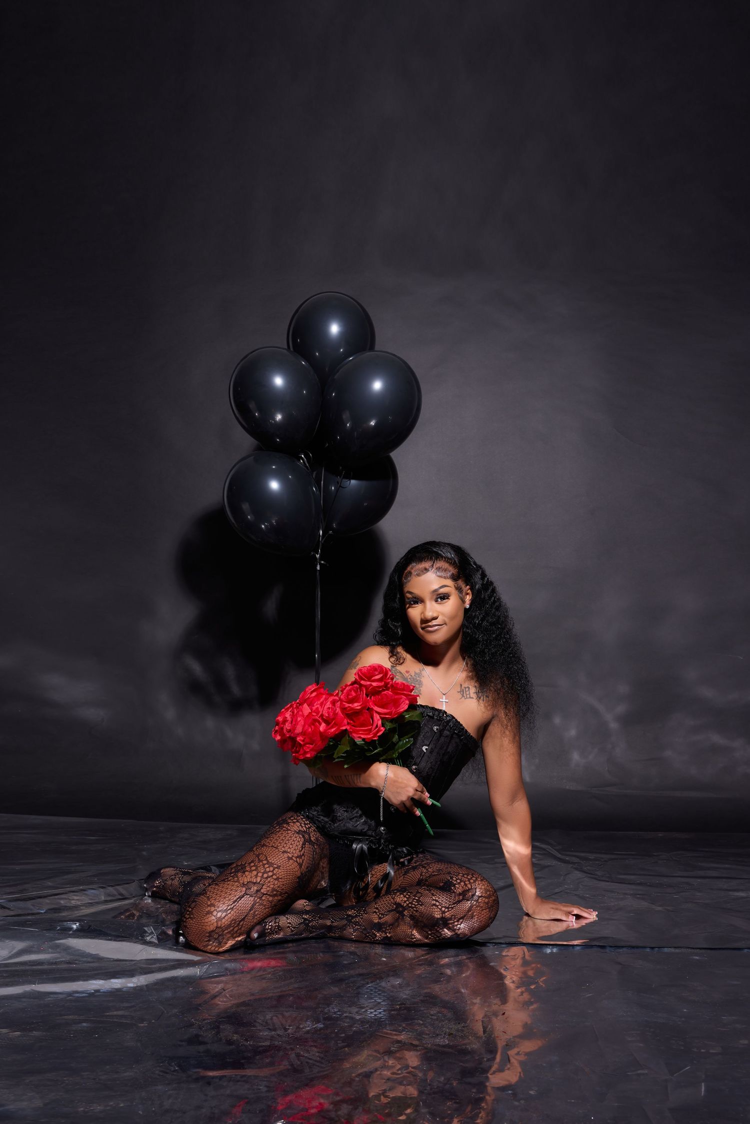 Dramatic scene with black balloons and red roses against dark floor.