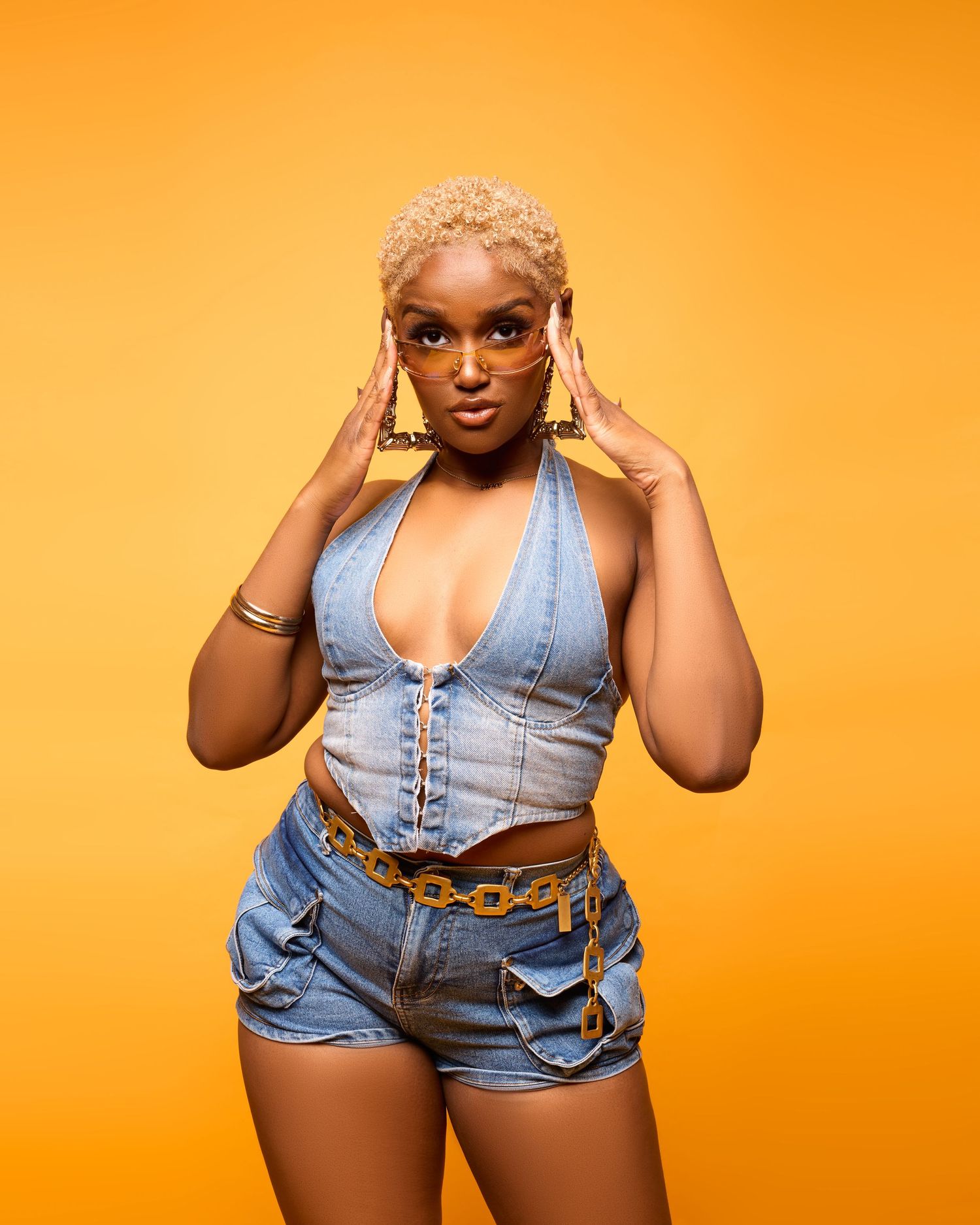 A model poses in a denim vest and shorts against a vibrant orange background in a fashion photoshoot series.