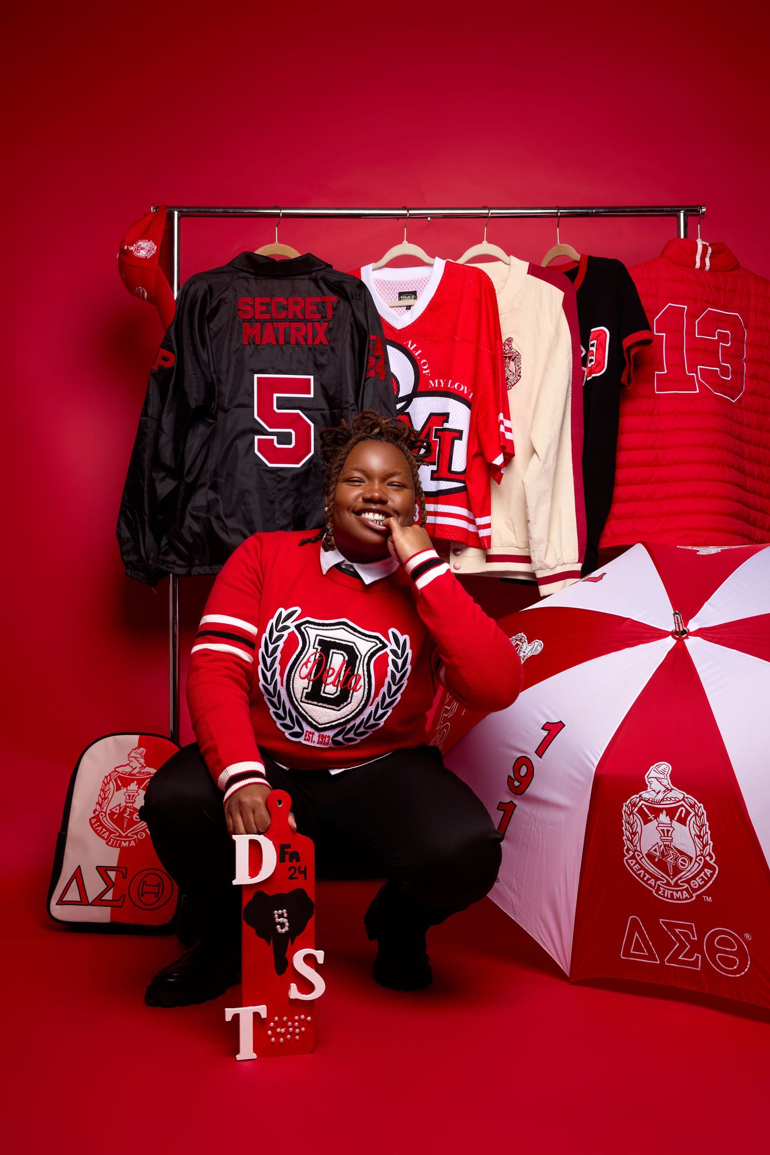 Graduation photo session with red backdrop featuring Delta Sigma Theta sorority letters and branded umbrella.