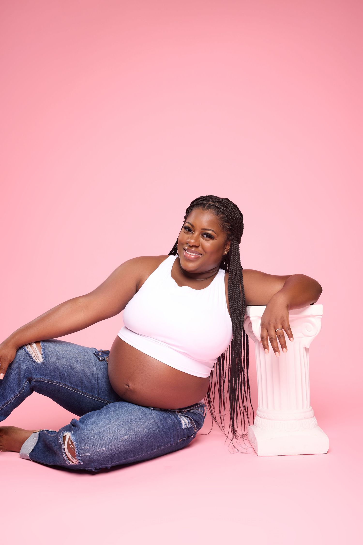 Relaxed maternity portraits against pink backdrop with casual styling and natural poses.
