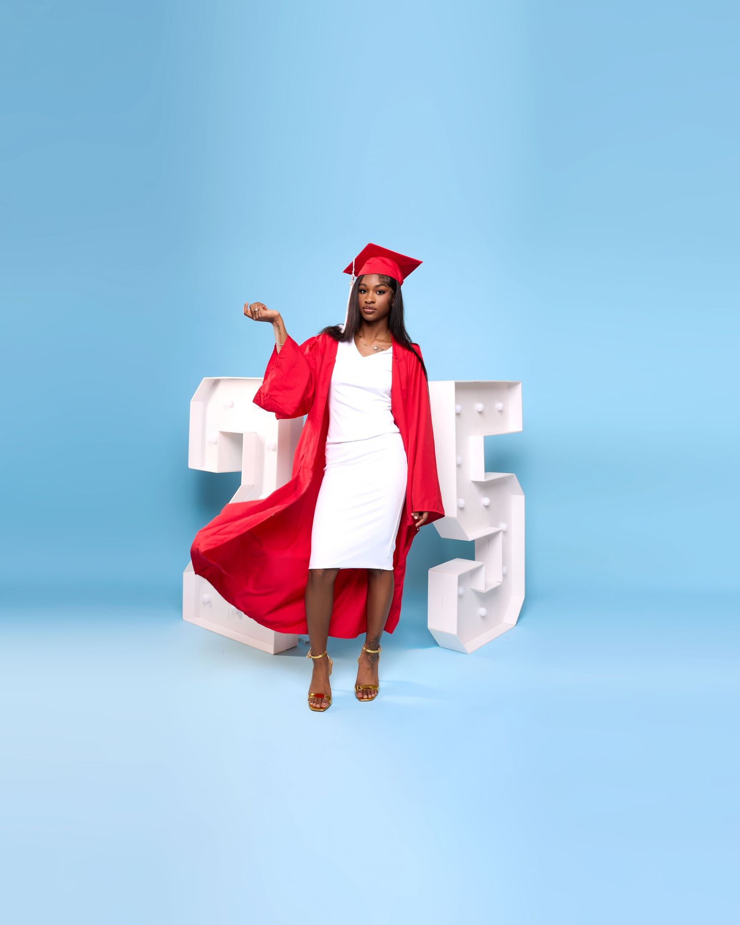 A graduate in red cap and gown poses with decorative numbers against a blue backdrop.