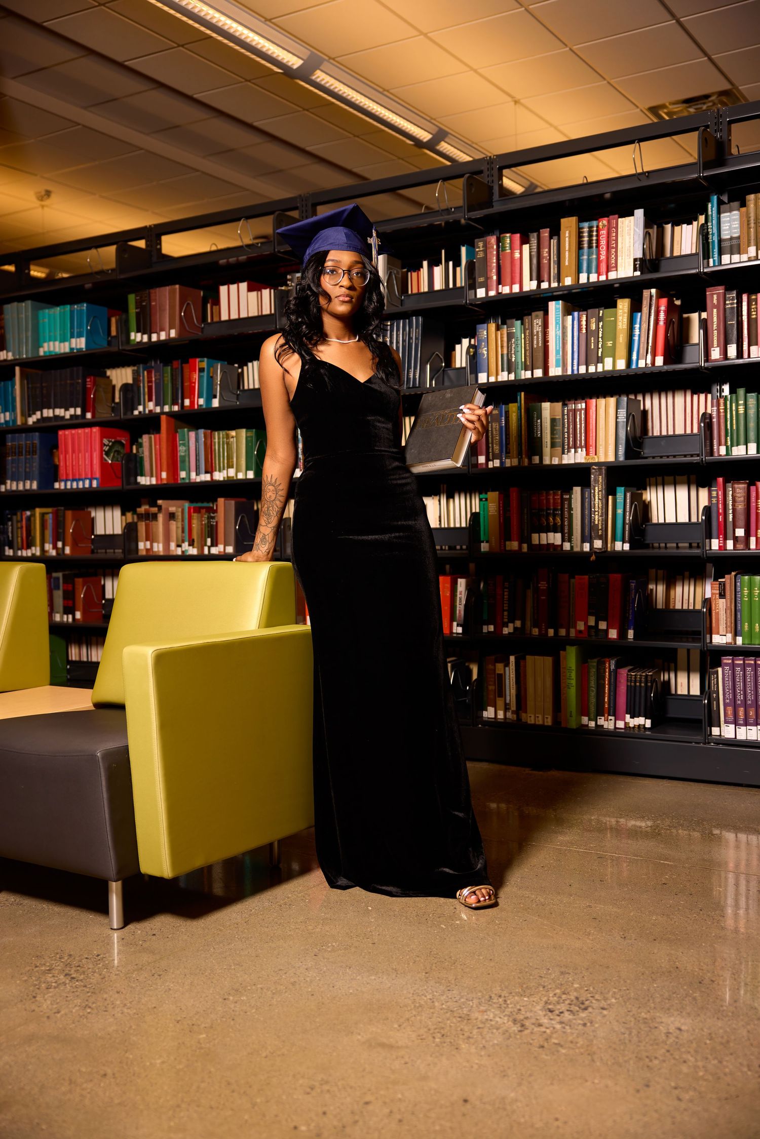 Library interior with yellow chairs and rows of bookshelves in warm lighting.