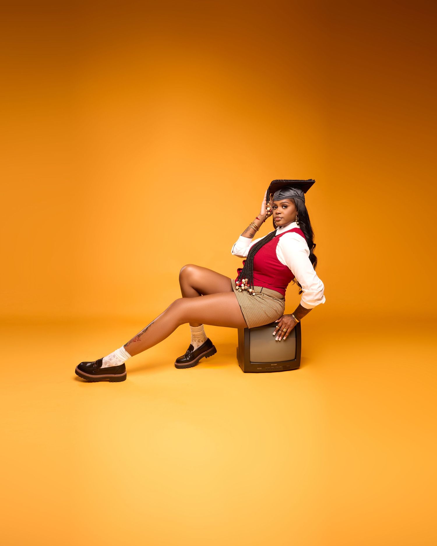 Graduate in academic attire poses laying down in artistic series against orange background.