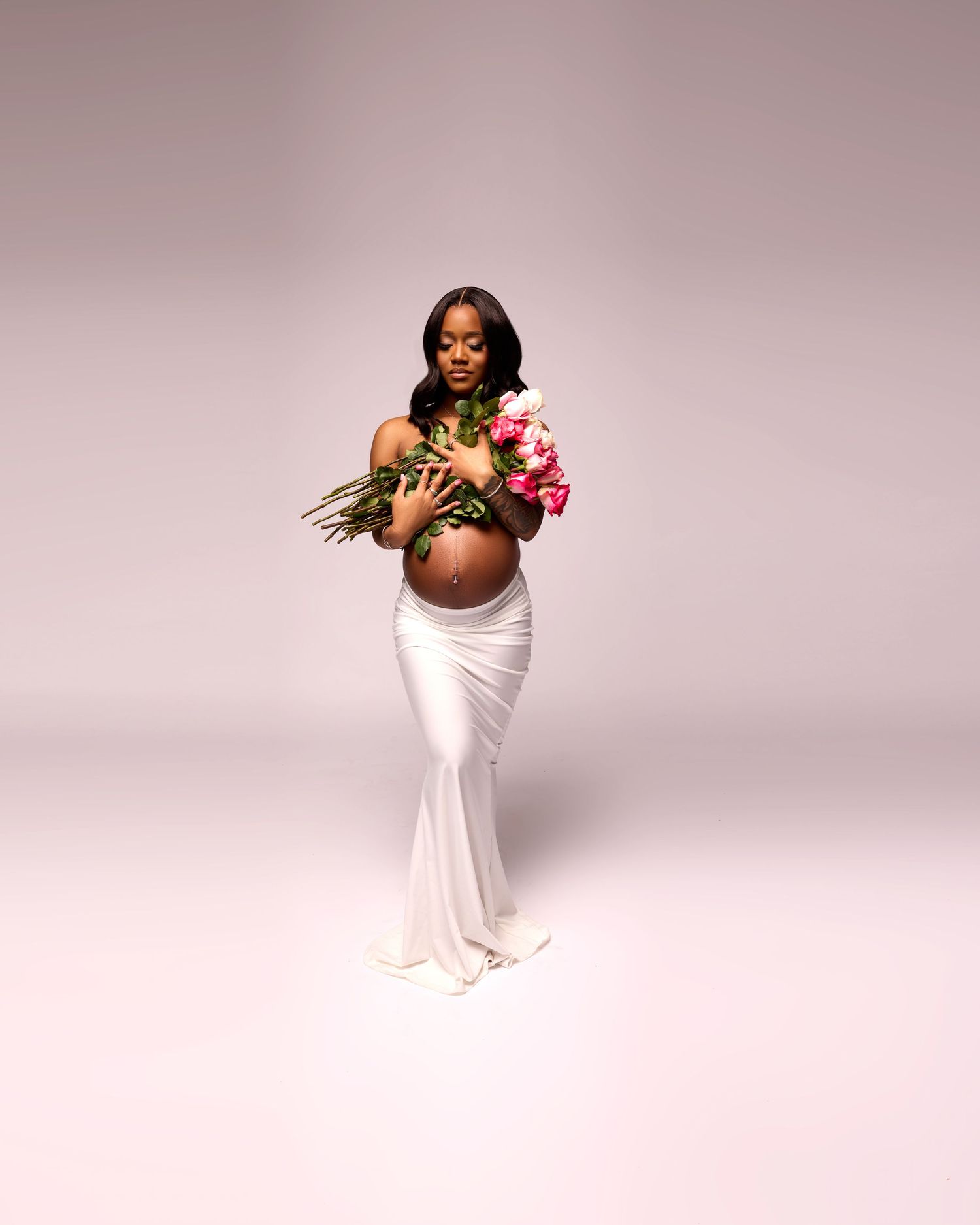 Elegant maternity portrait with woman in white dress holding pink roses.
