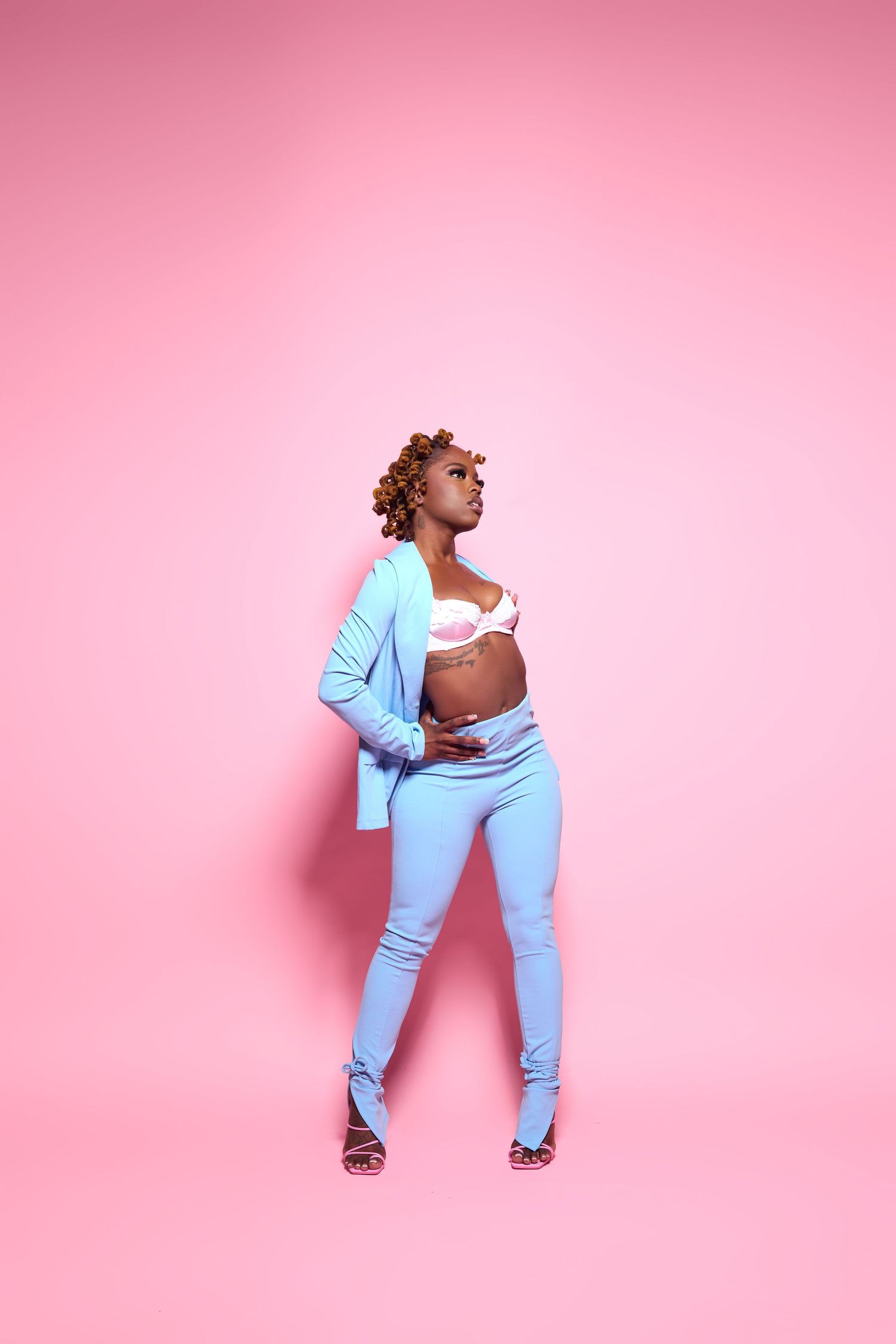 Stylish poses in powder blue ensemble against pink studio backdrop.