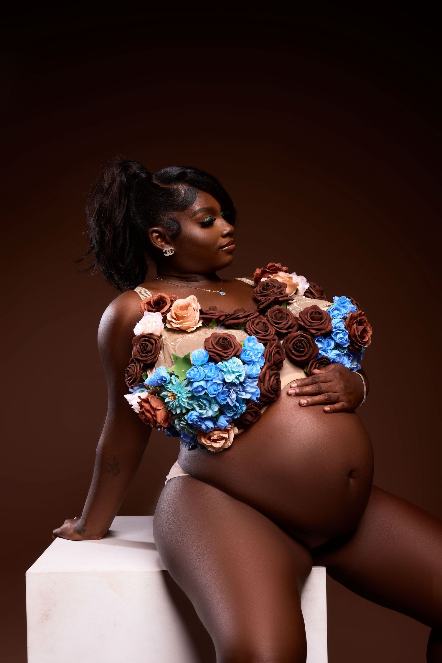Artistic maternity photo featuring floral decorations in blue and peach tones against a dark brown background.