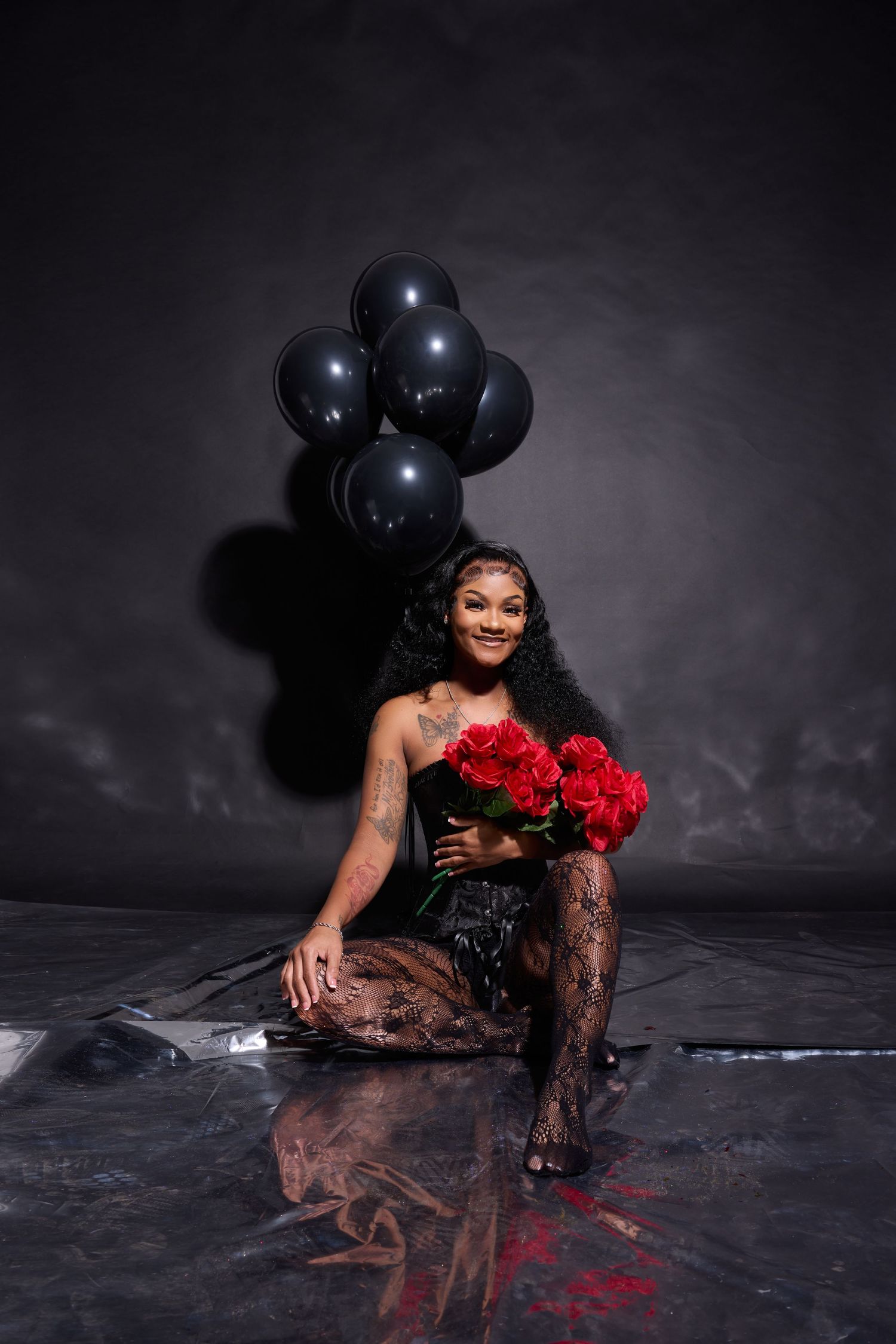 Dramatic photoshoot with black balloons and red roses on reflective dark floor.