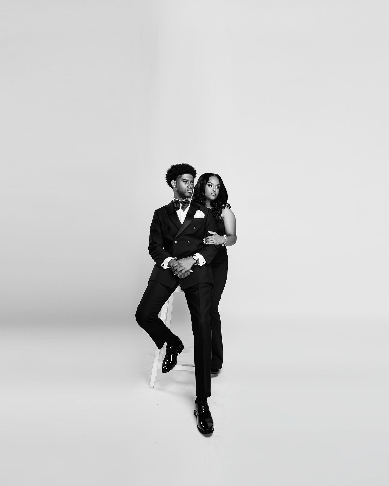 Couple in formal attire performs dynamic dance moves against white background.
