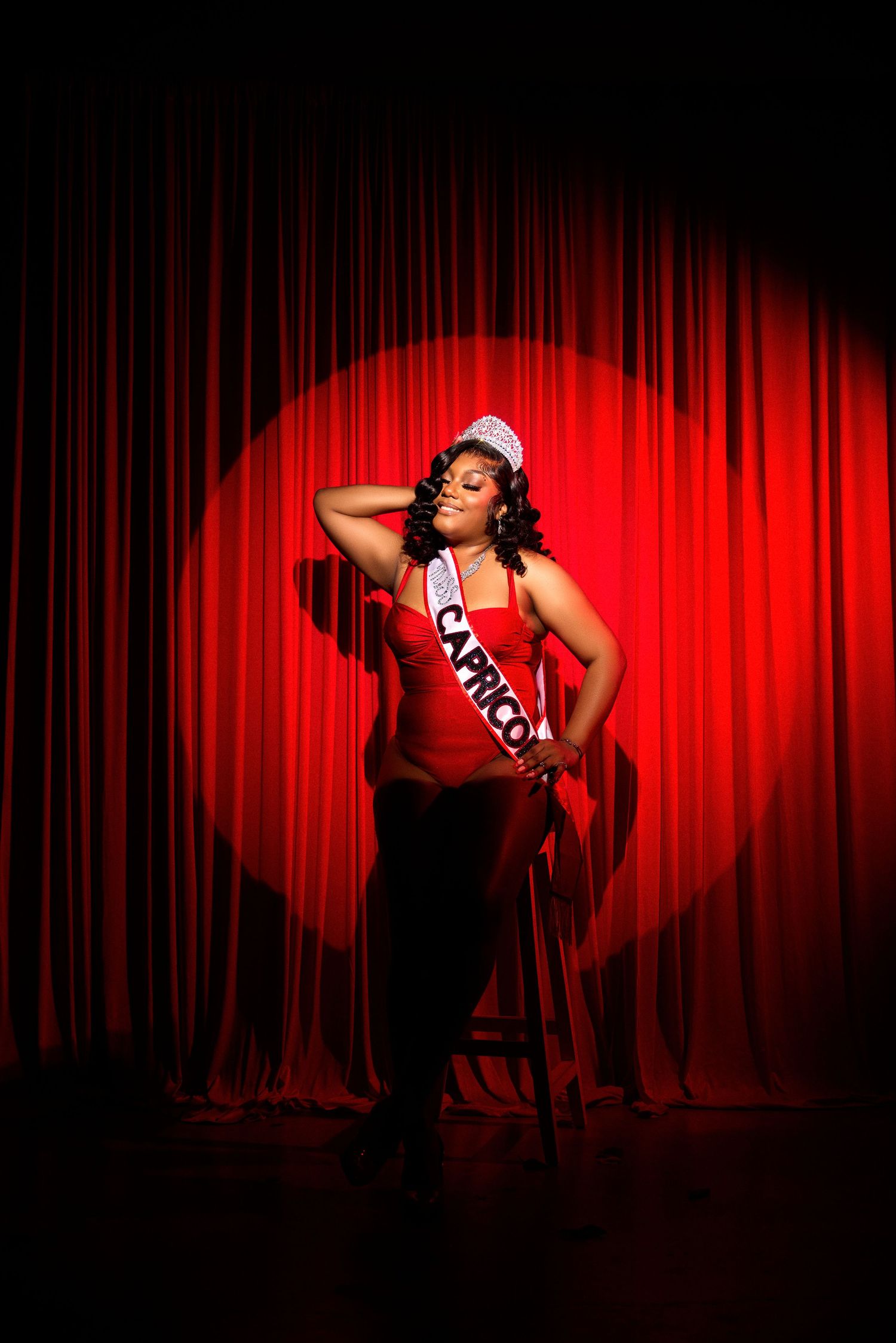 Dramatic portrait against red curtain backdrop with theatrical spotlight creating moody ambiance.