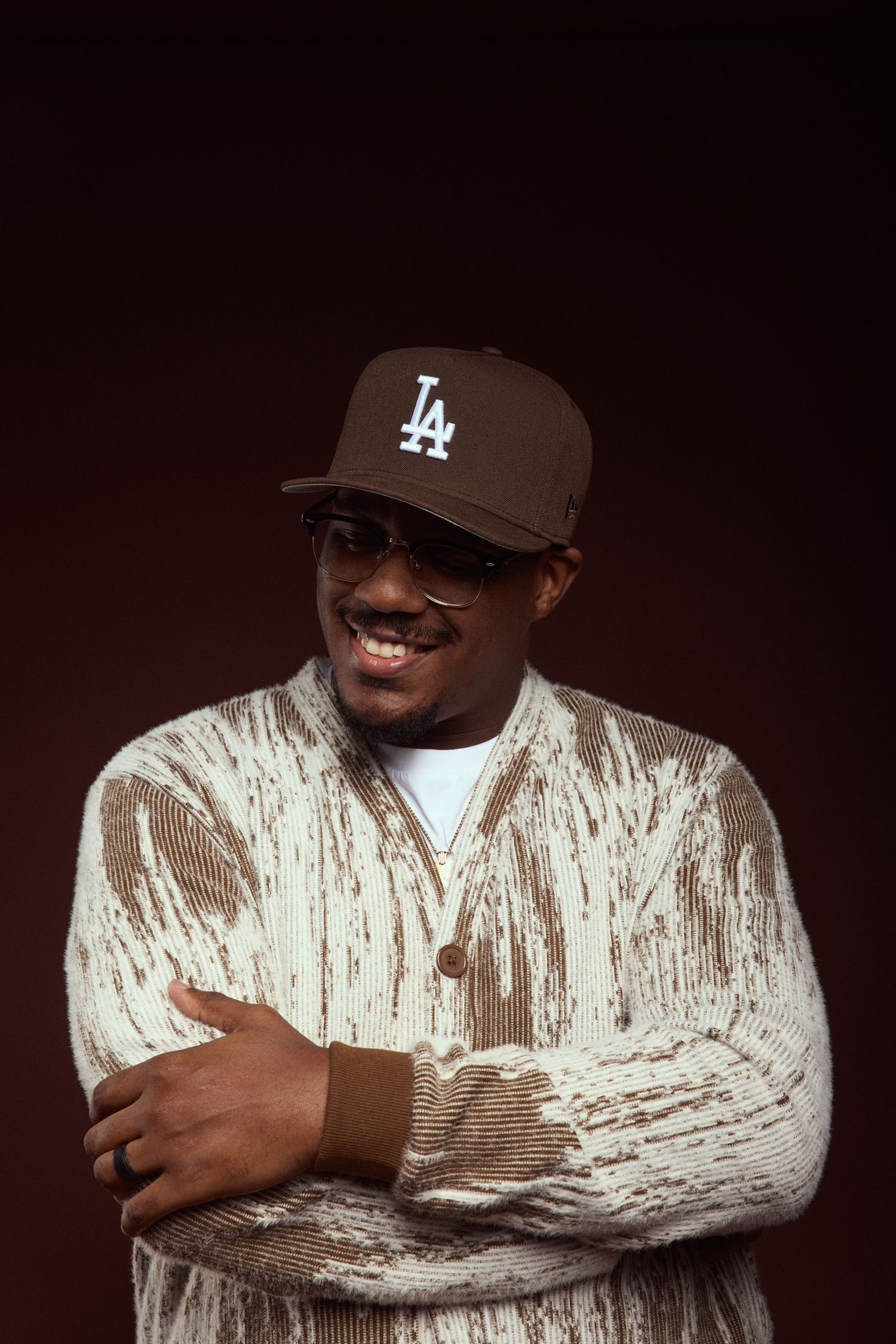 Studio portraits in LA baseball cap and textured white jacket against dark background.