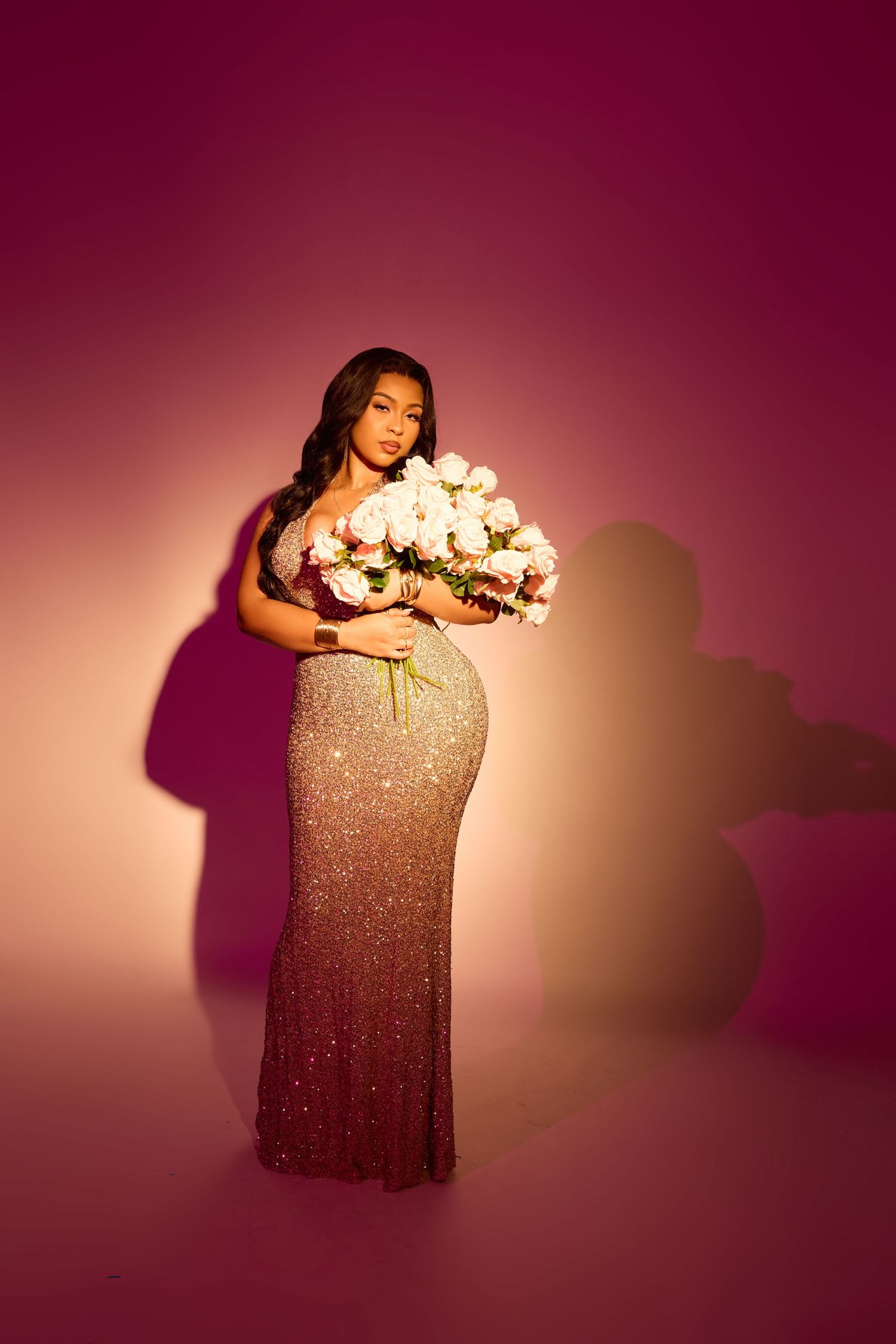 A glittering silver evening gown catches the light in a romantic burgundy-tinted studio photoshoot with white roses.