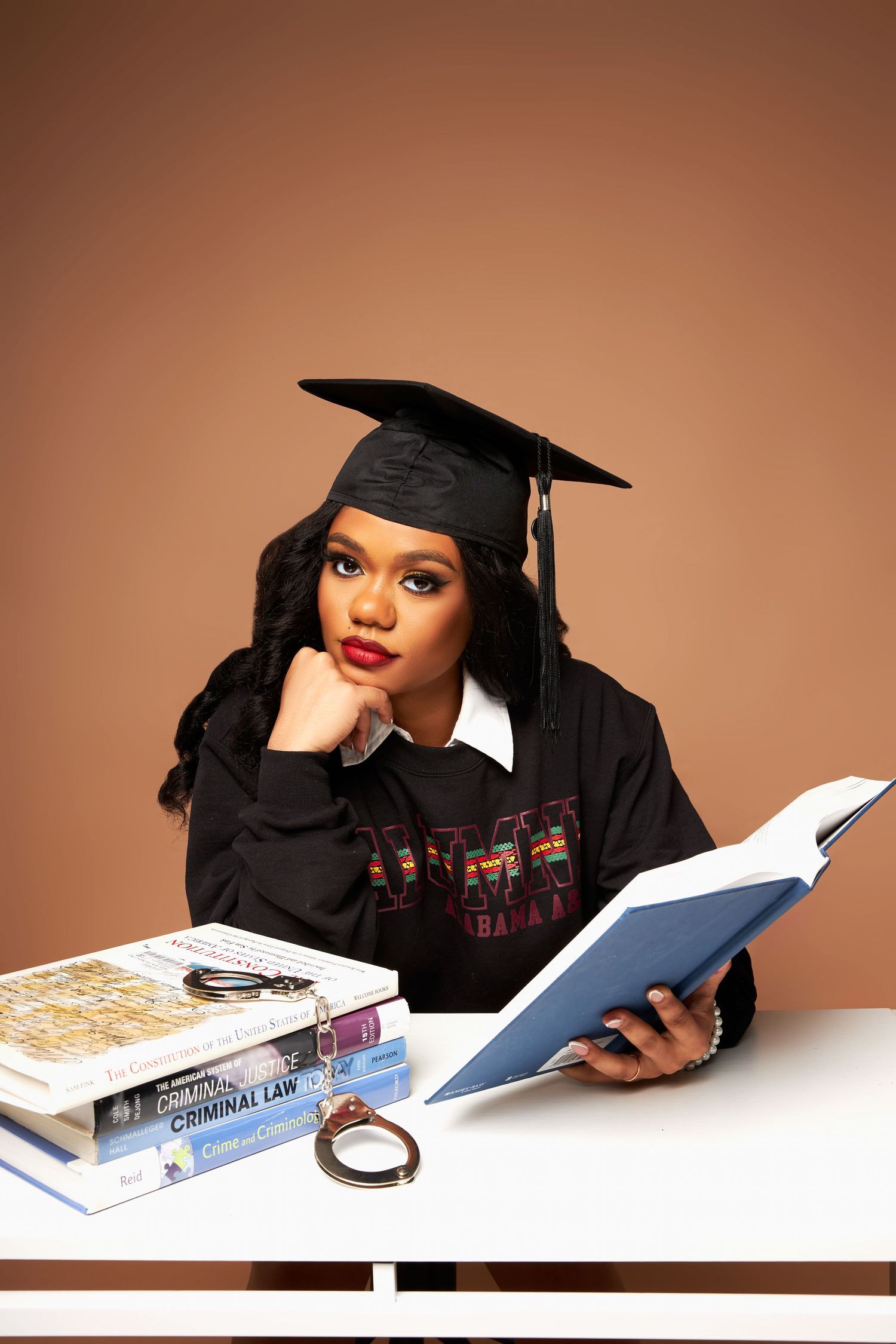 Student in graduation attire lies on floor reading books in professional photo series.