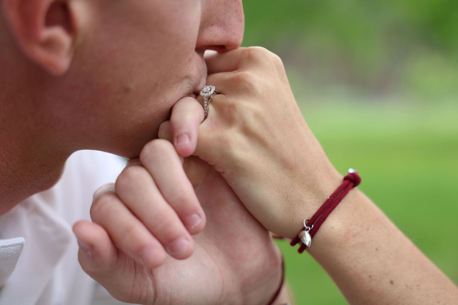 Close-up shot of someone gently kissing their own fingers while wearing a white shirt outdoors.