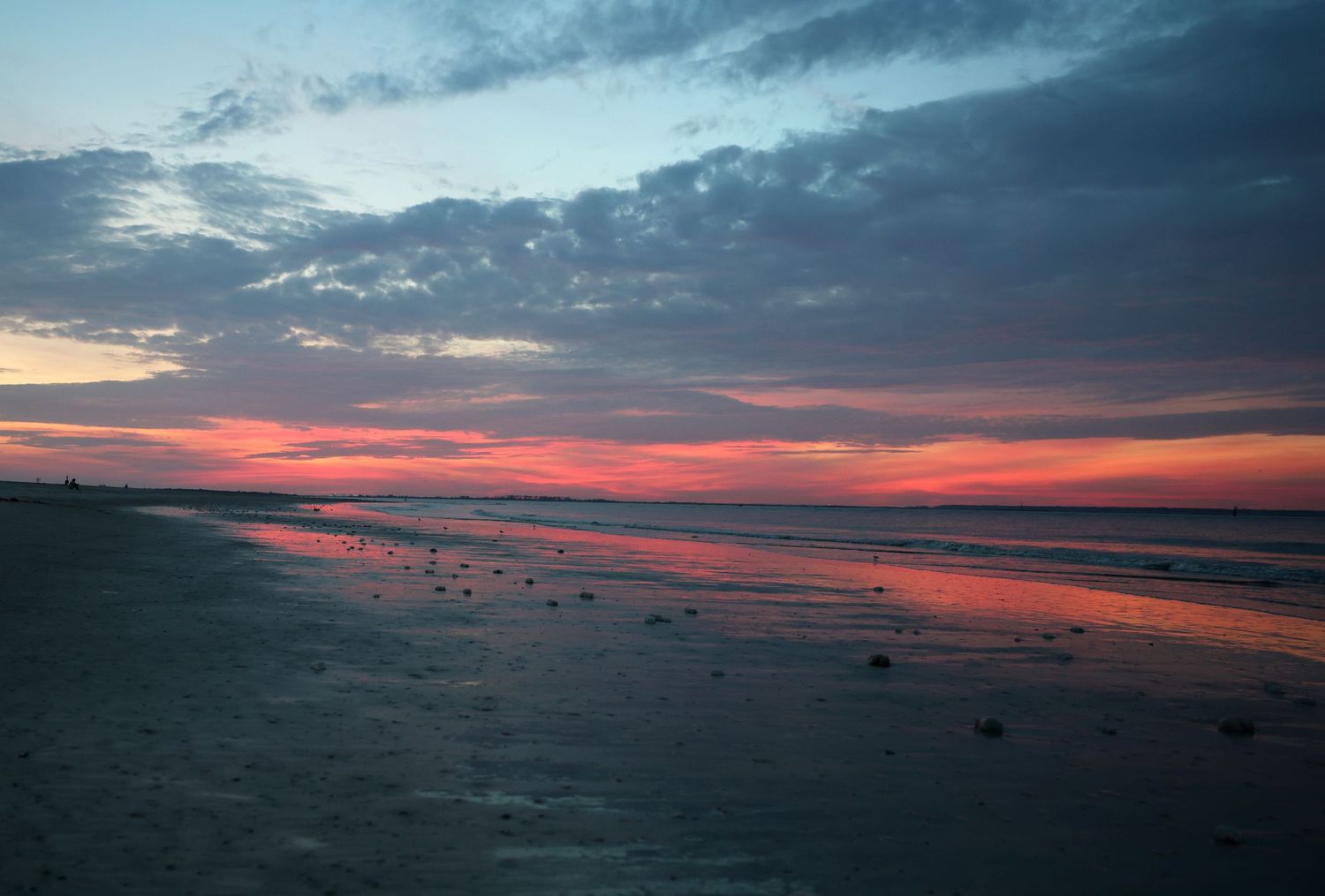 Dramatic sunset creates red and orange reflections on a dark beach at dusk.