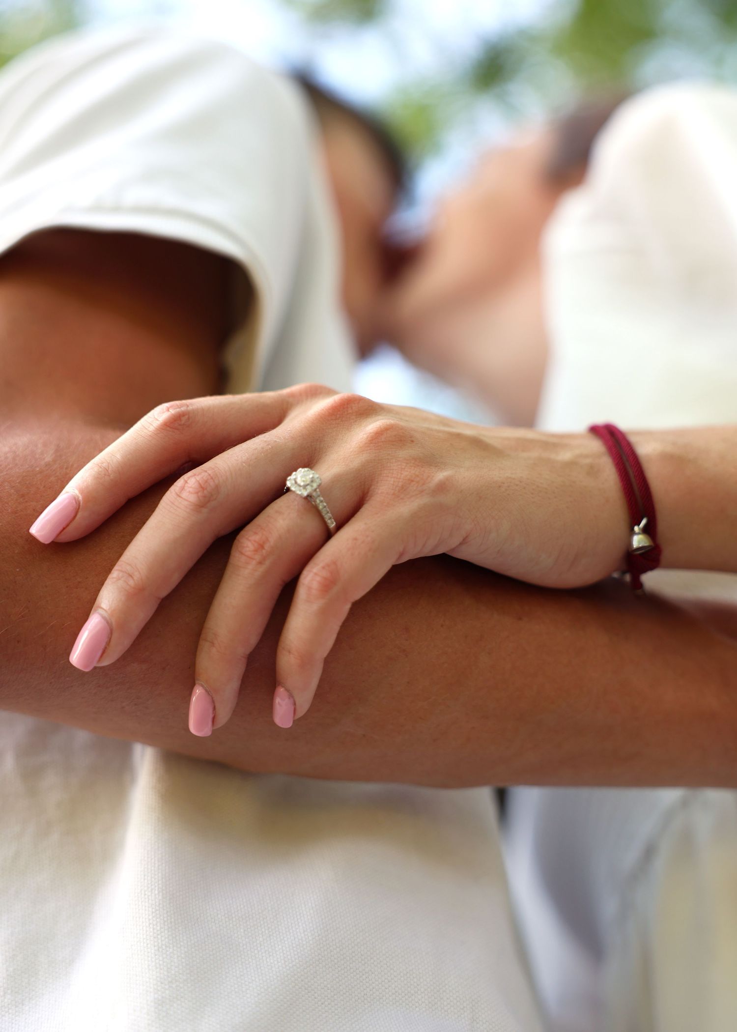 Hand with pink nails and diamond ring resting gently on an arm.