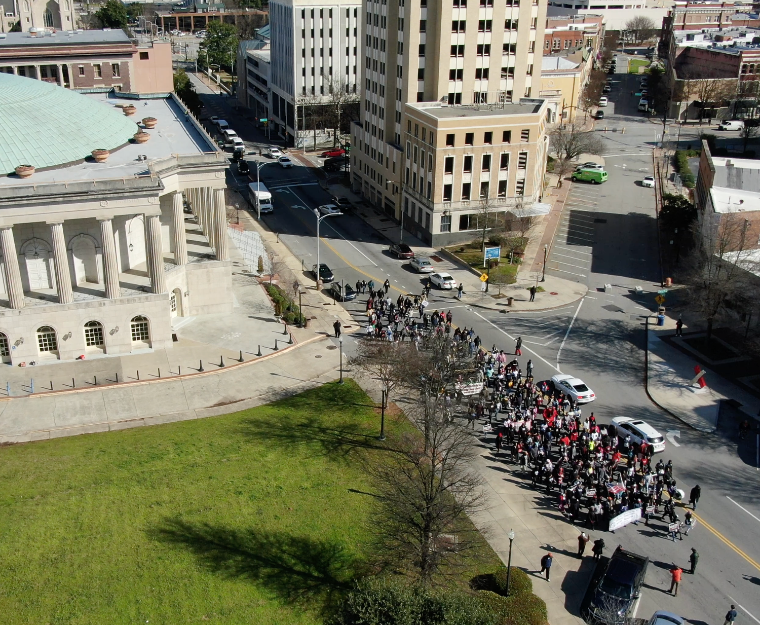 Aerial shot of city street corner with large crowd forming a queue next to grassy area.