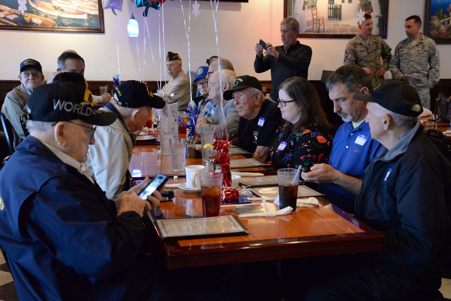 People gathered around tables in a restaurant with blue lighting and decorative artwork on the walls. World War II commemoration event.