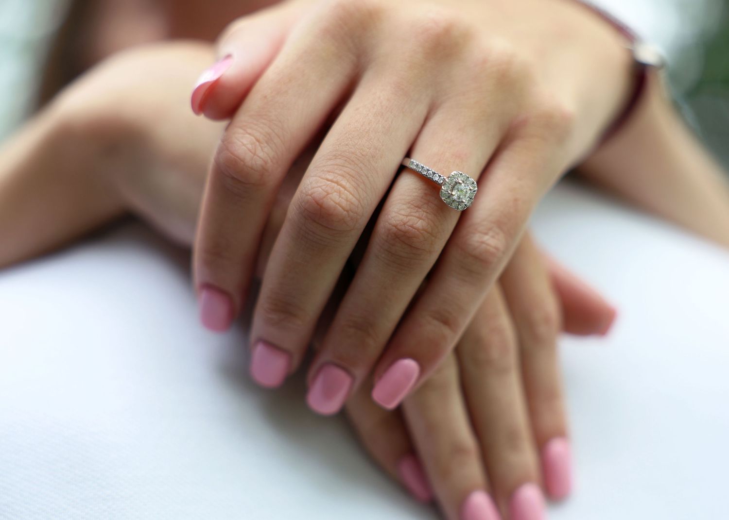 Close-up of hands with pink manicured nails showing off a sparkling diamond engagement ring.