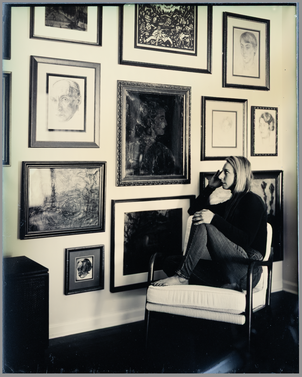 Black and white panoramic photograph showing a gallery wall filled with framed artwork and photographs.