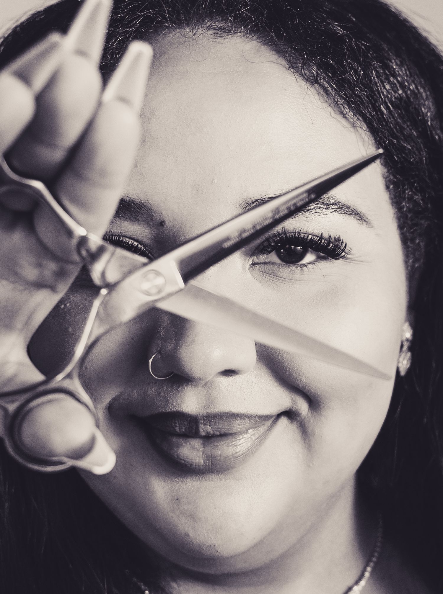 Close-up black and white photo of hairstyling scissors held in front of face.