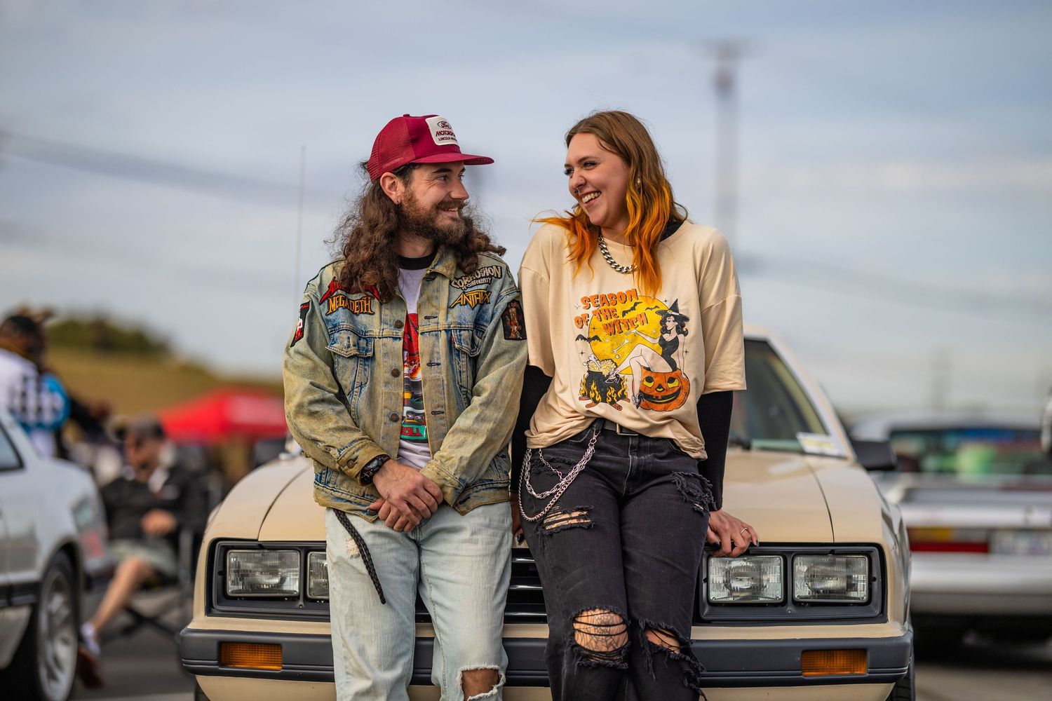 Couple sitting in back of pickup truck sharing drinks and snacks at sunset in casual outdoor setting.