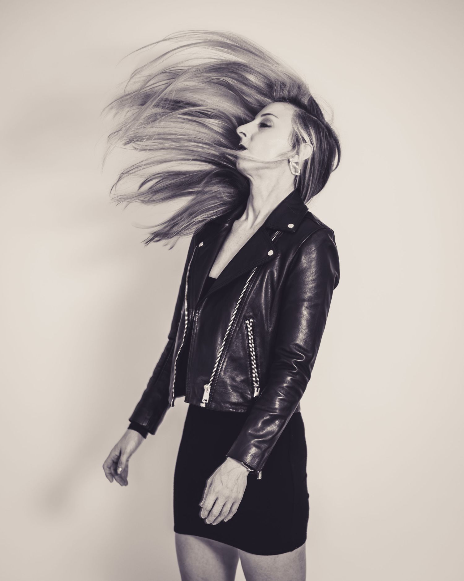 Dynamic black and white portrait with flowing hair and leather jacket against white background.