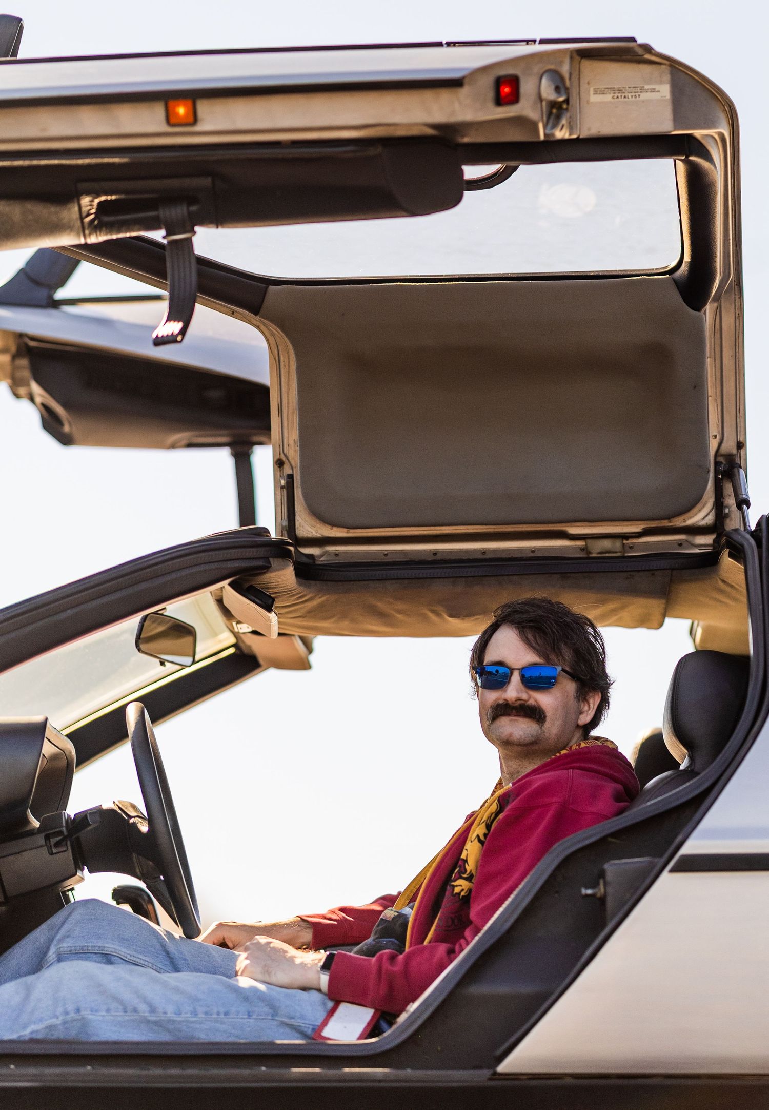 A vintage DeLorean sports car with its iconic gull-wing door raised at an outdoor event.