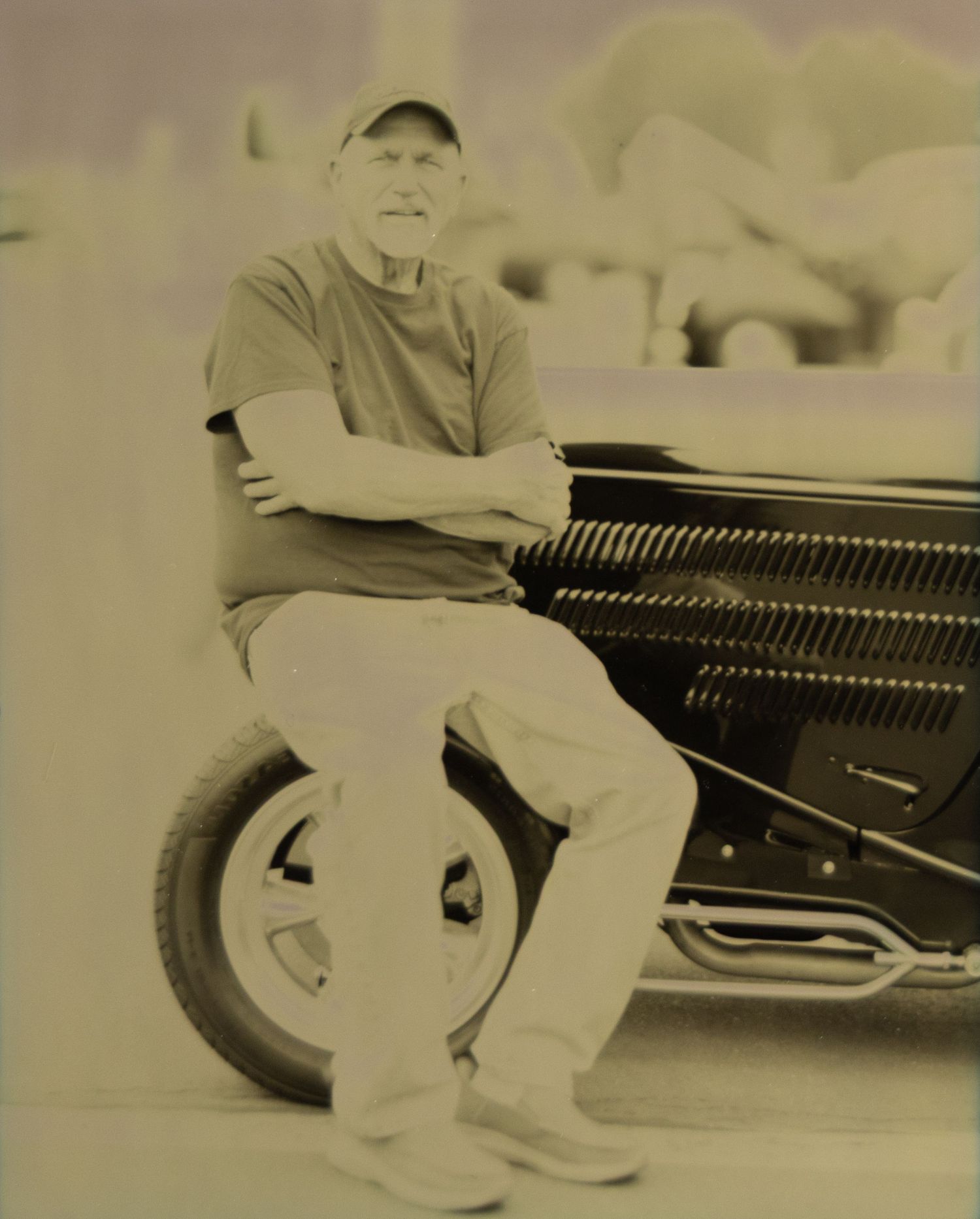 Man leaning on vintage black car in sepia-toned outdoor photo.