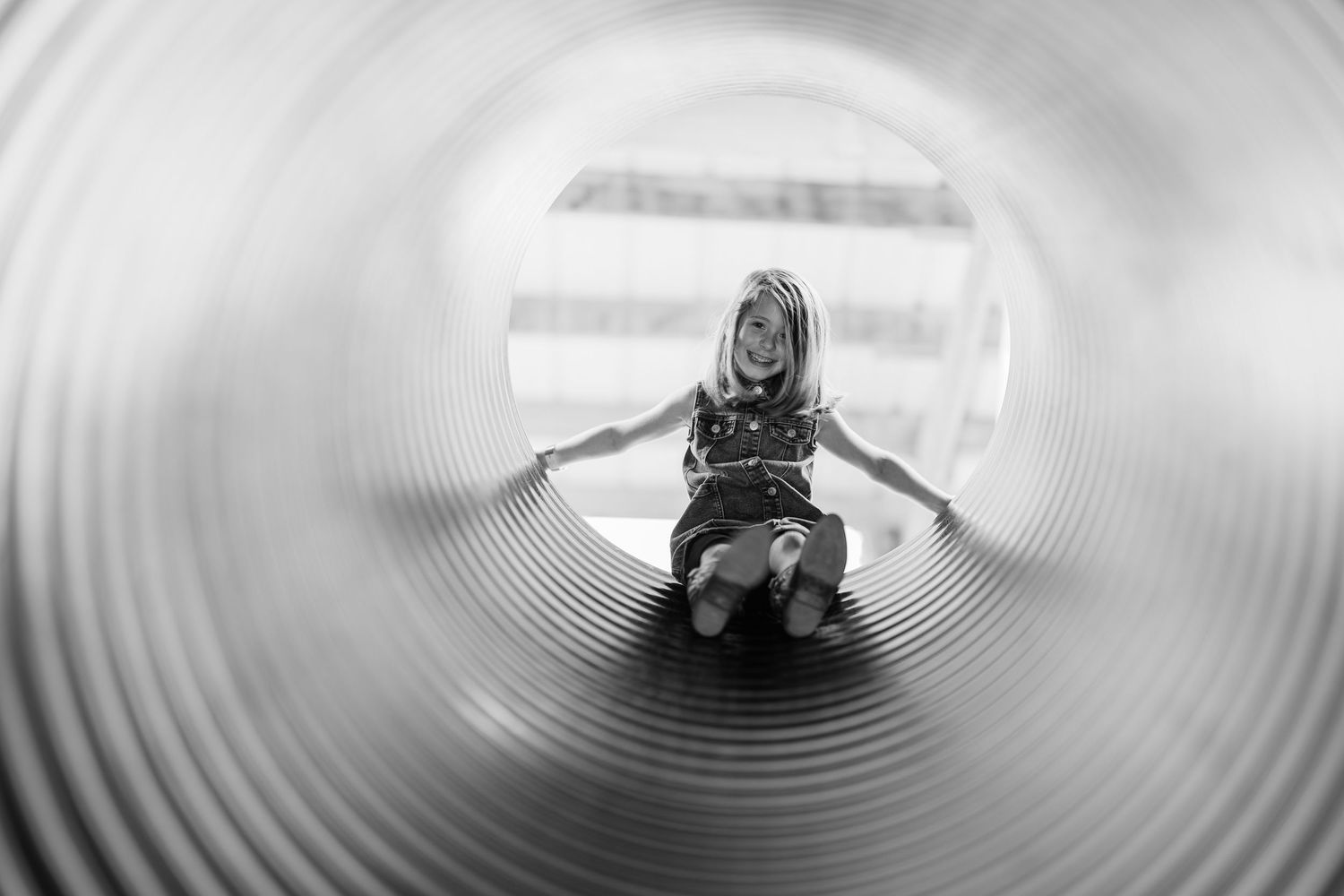 Child sliding through a circular tunnel slide, captured in black and white with spiral perspective.