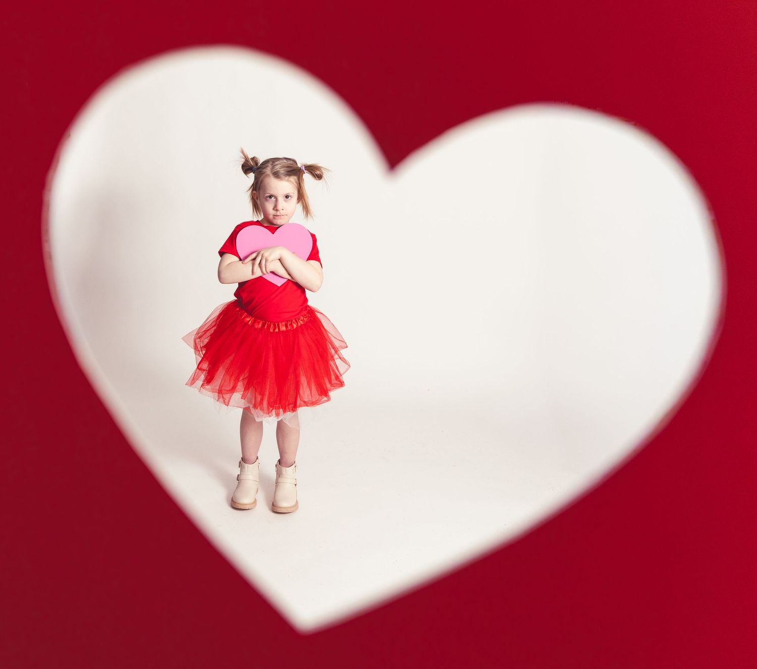 Heart-shaped photo collage with red and white frames showing a young child in a tulle dress and pigtails.