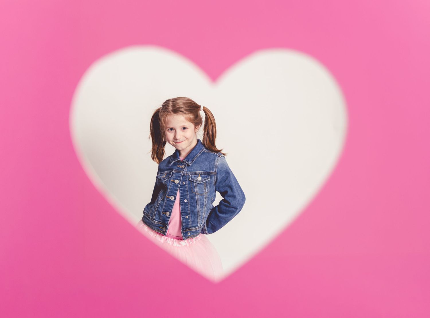 A person peeks through a heart-shaped cutout against a bright pink background in a creative Valentine's Day photo series.