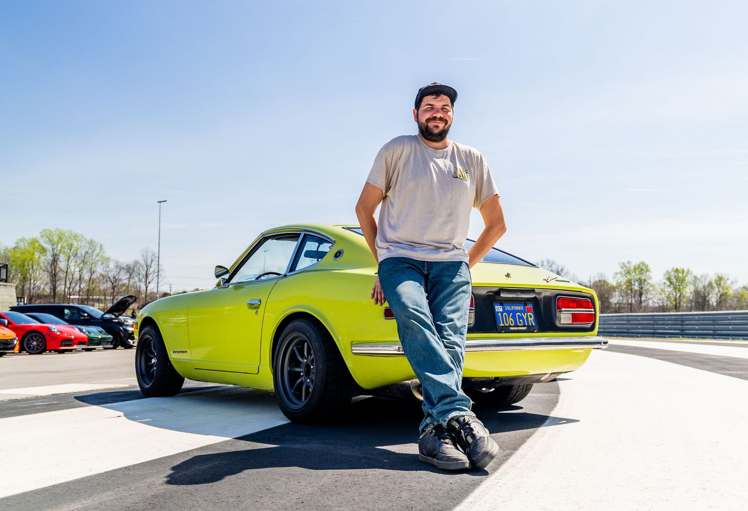 Man posing in front of a bright green classic Datsun 240Z sports car on a sunny day at a car meet.