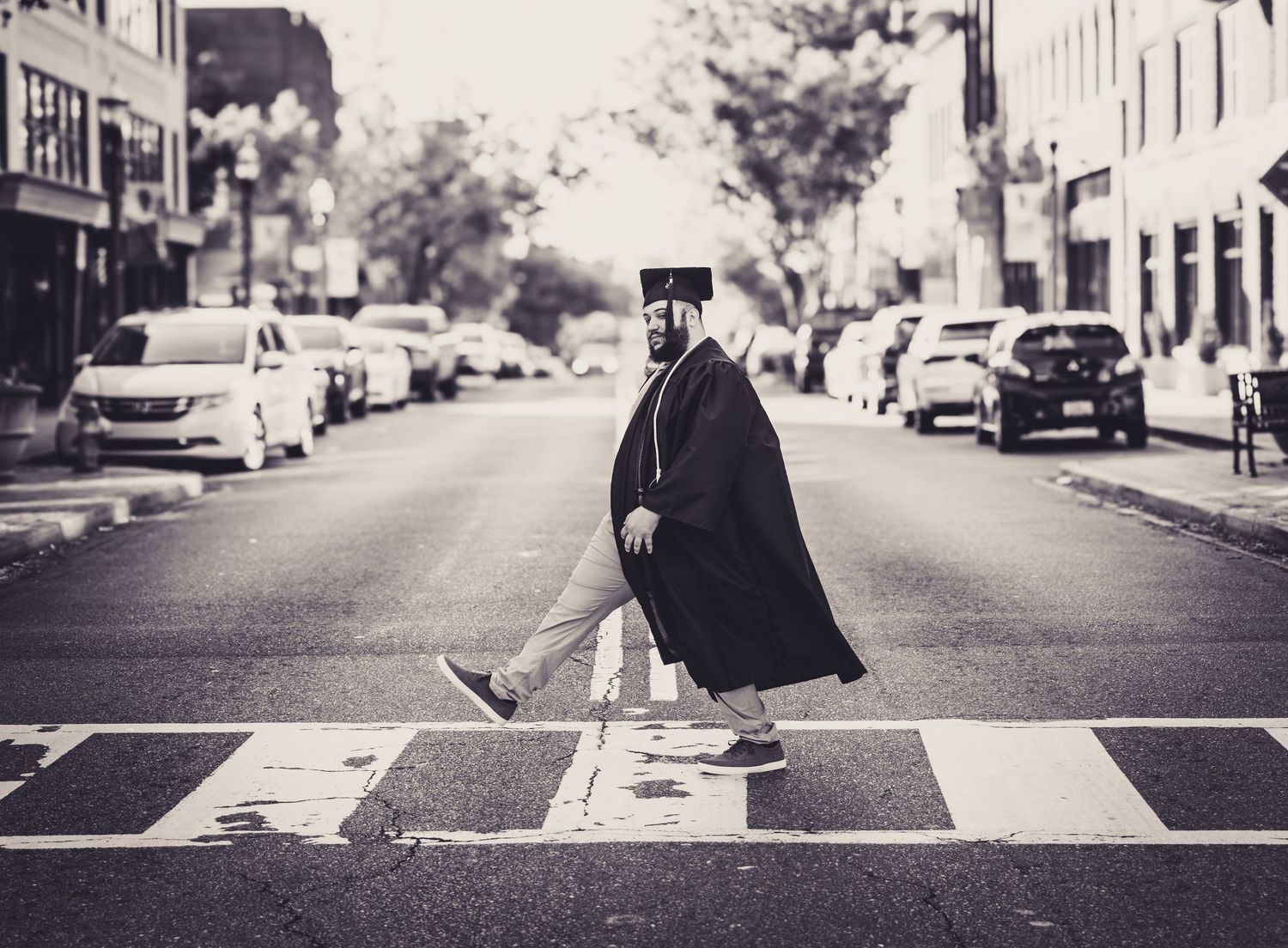 Graduate in cap and gown crossing a street in black and white urban photography.