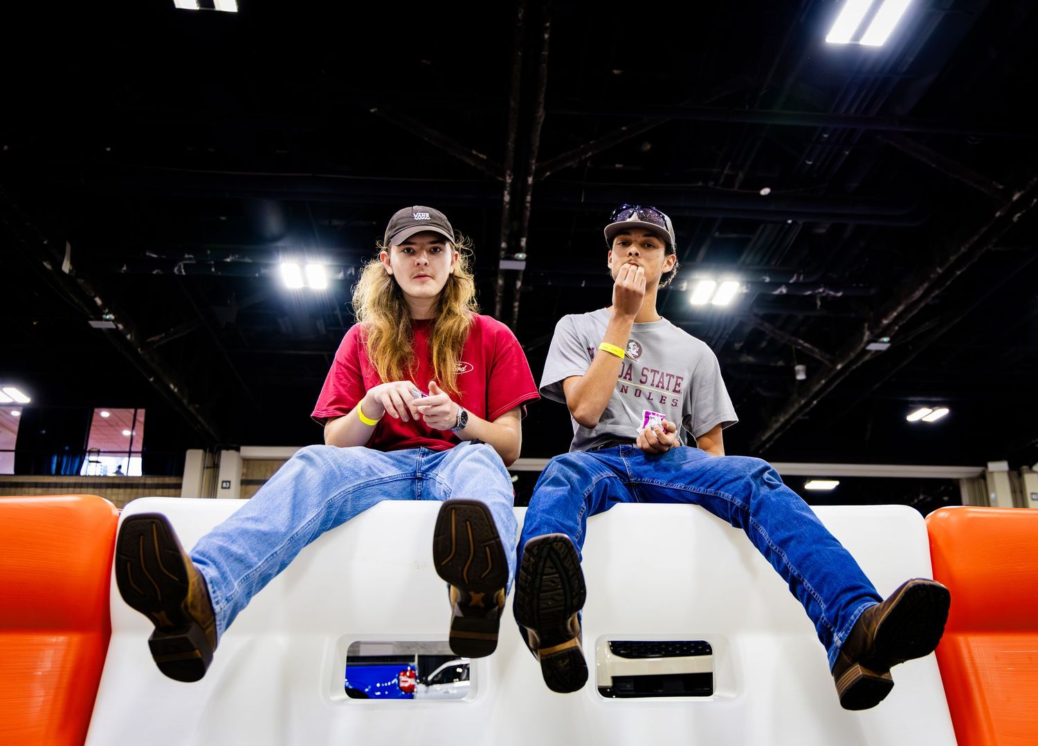 People sitting on a white platform in an indoor venue with overhead lighting.
