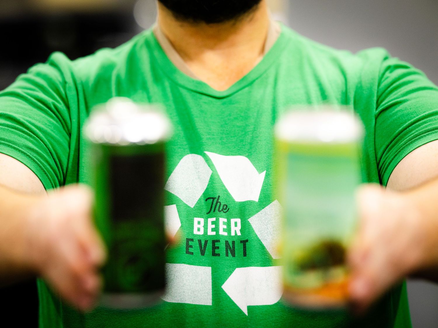 A green t-shirt with recycling beer event logo shown holding dark beer glasses.