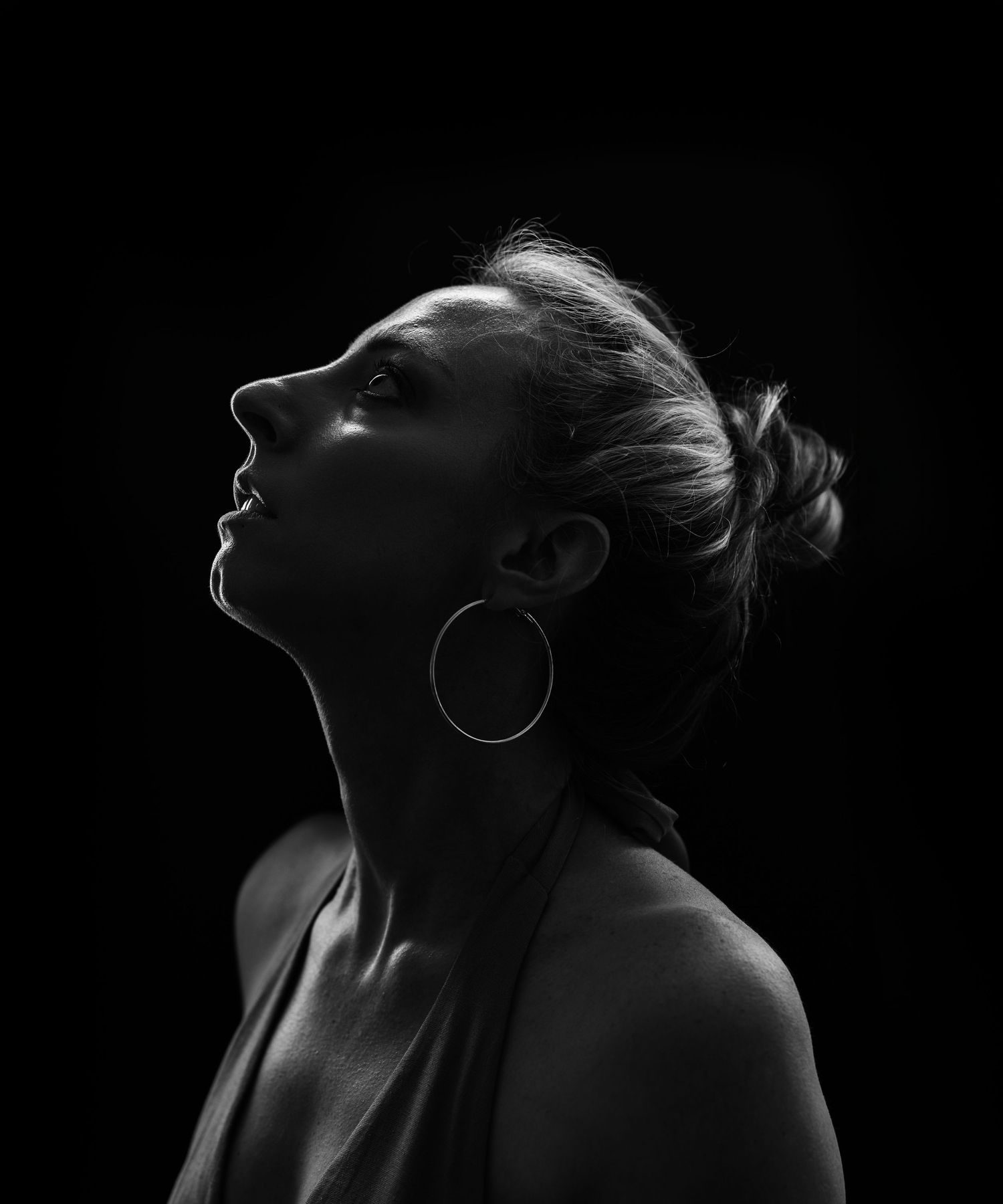 Black and white profile portrait of a woman with hoop earrings looking upward against dark background.