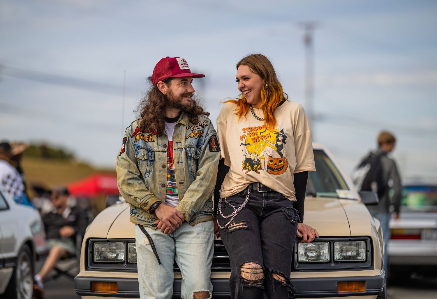 A couple sitting on vintage car at outdoor event sharing a casual moment together.