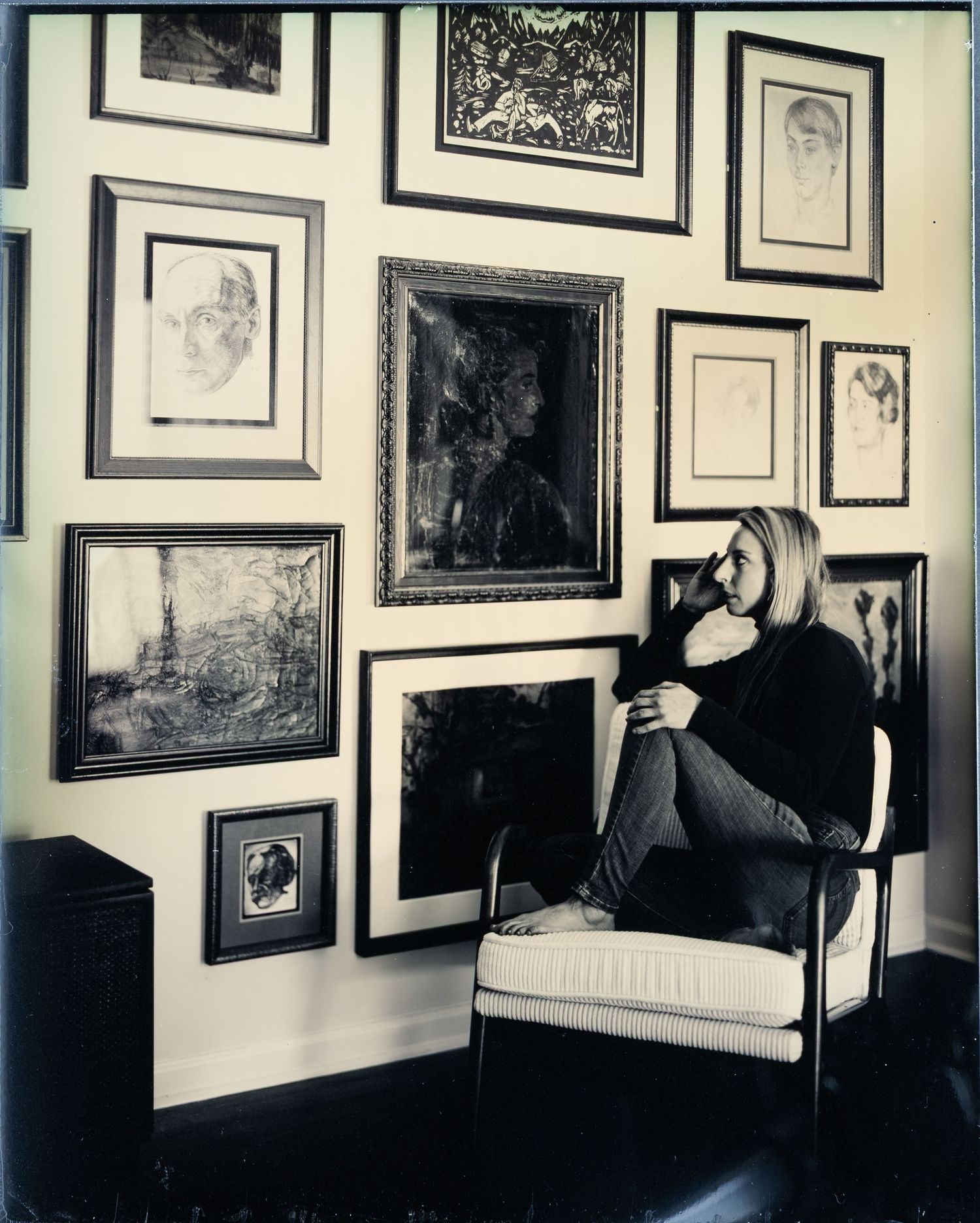 Black and white photograph showing a gallery wall filled with framed artwork and portraits in an elegant interior space.