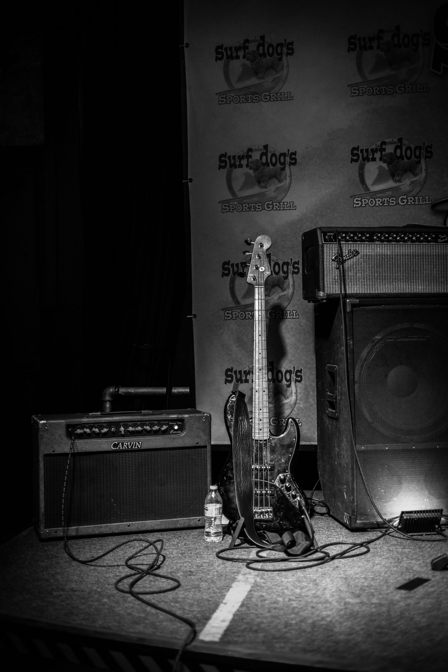 Black and white photo of guitar amplifiers and equipment setup on stage.