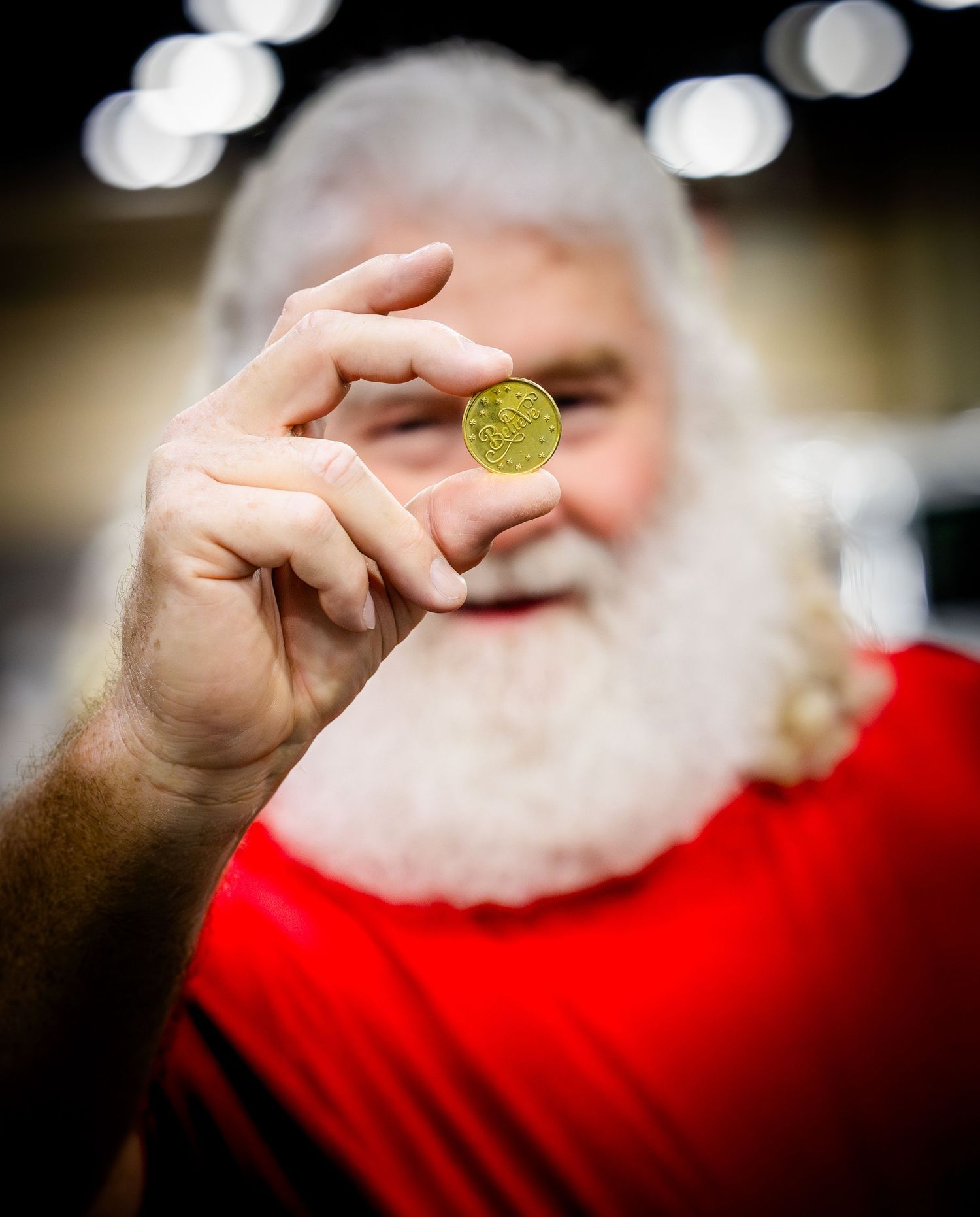 Someone in a red outfit holding up a golden Bitcoin cryptocurrency coin with a blurred background.