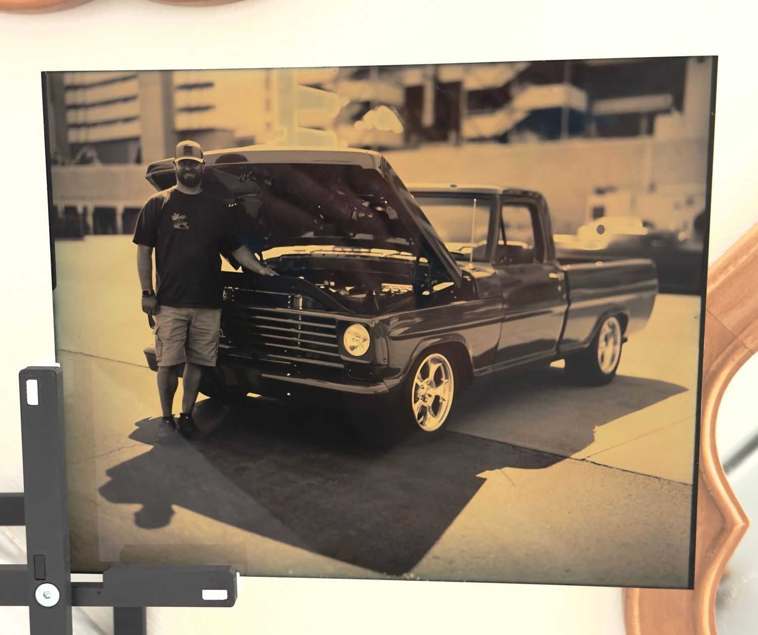 Man standing beside a custom black vintage Ford pickup truck with open hood at an outdoor car show.