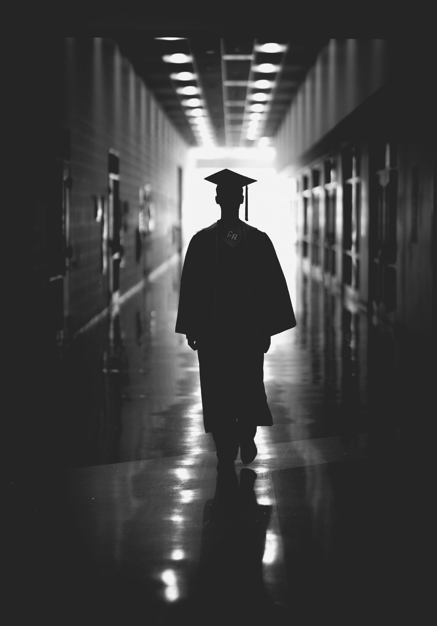Silhouette of a graduate in cap and gown walking down a dark hallway toward bright light.