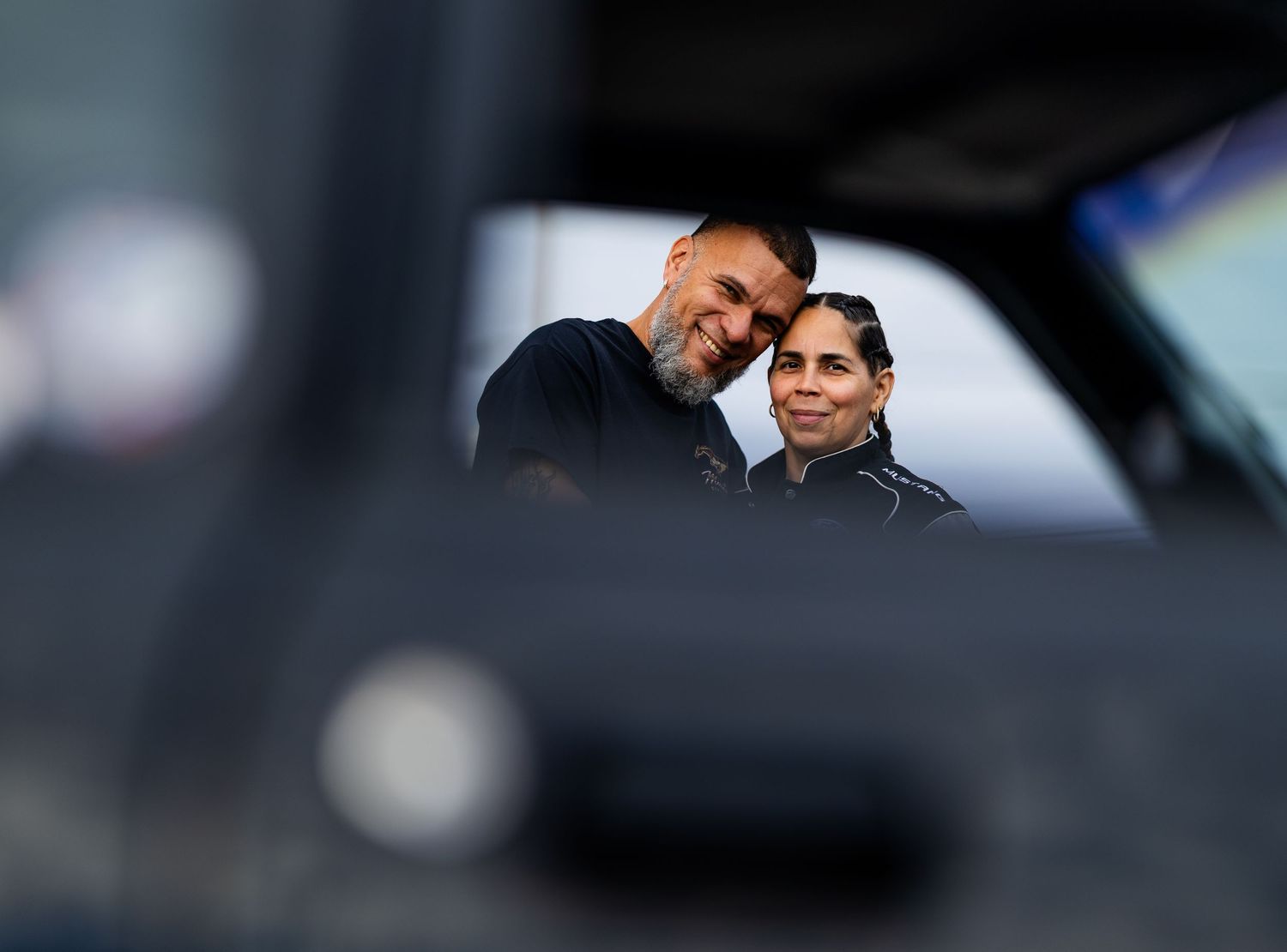 Candid shot through car window of two people having conversation at automotive event.